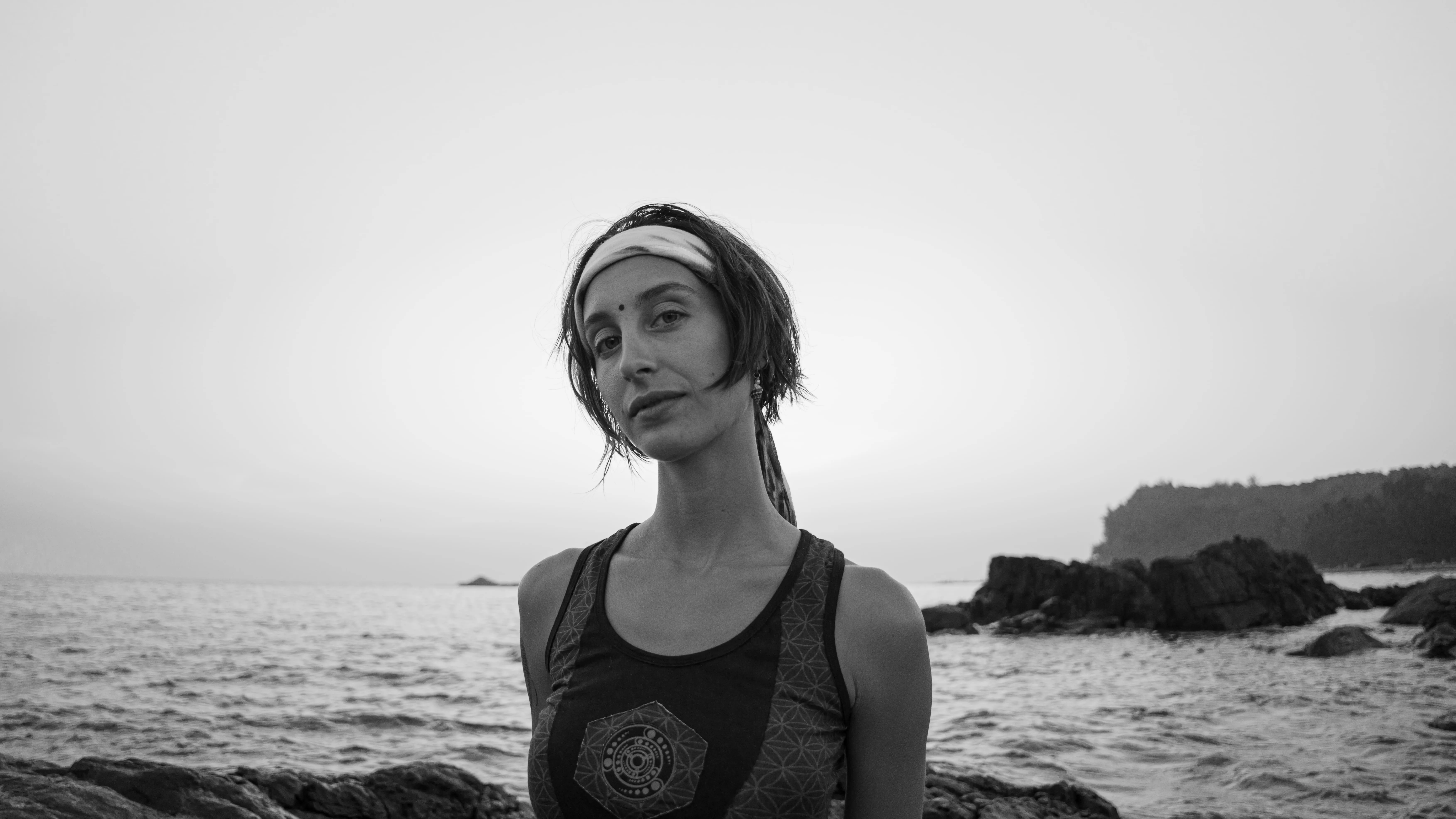 Black-and-white portrait of a woman in a patterned tank top beside the sea in Goa.