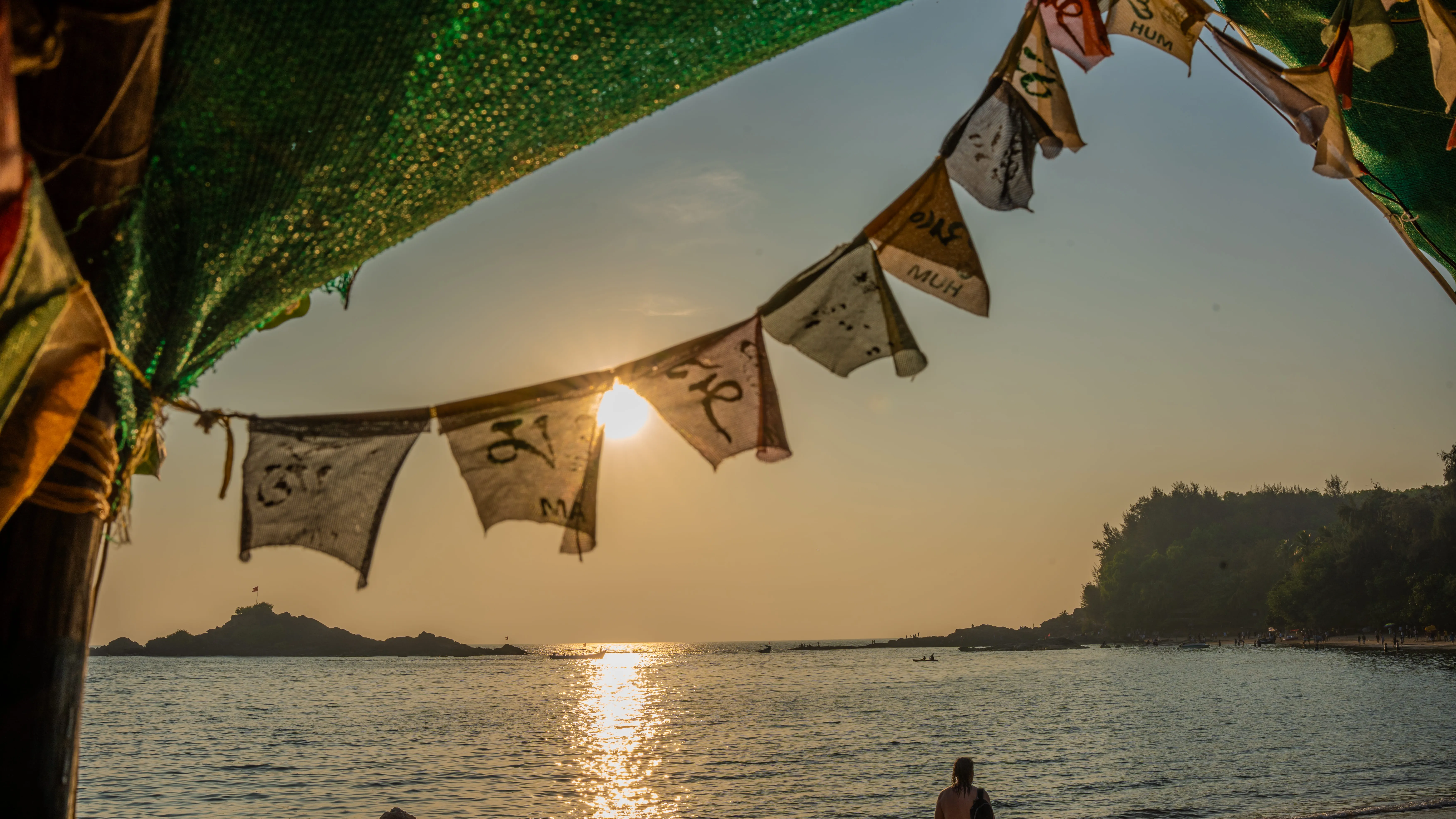 Sunset over the sea beneath a green canopy and hanging flags on a Goa beach.