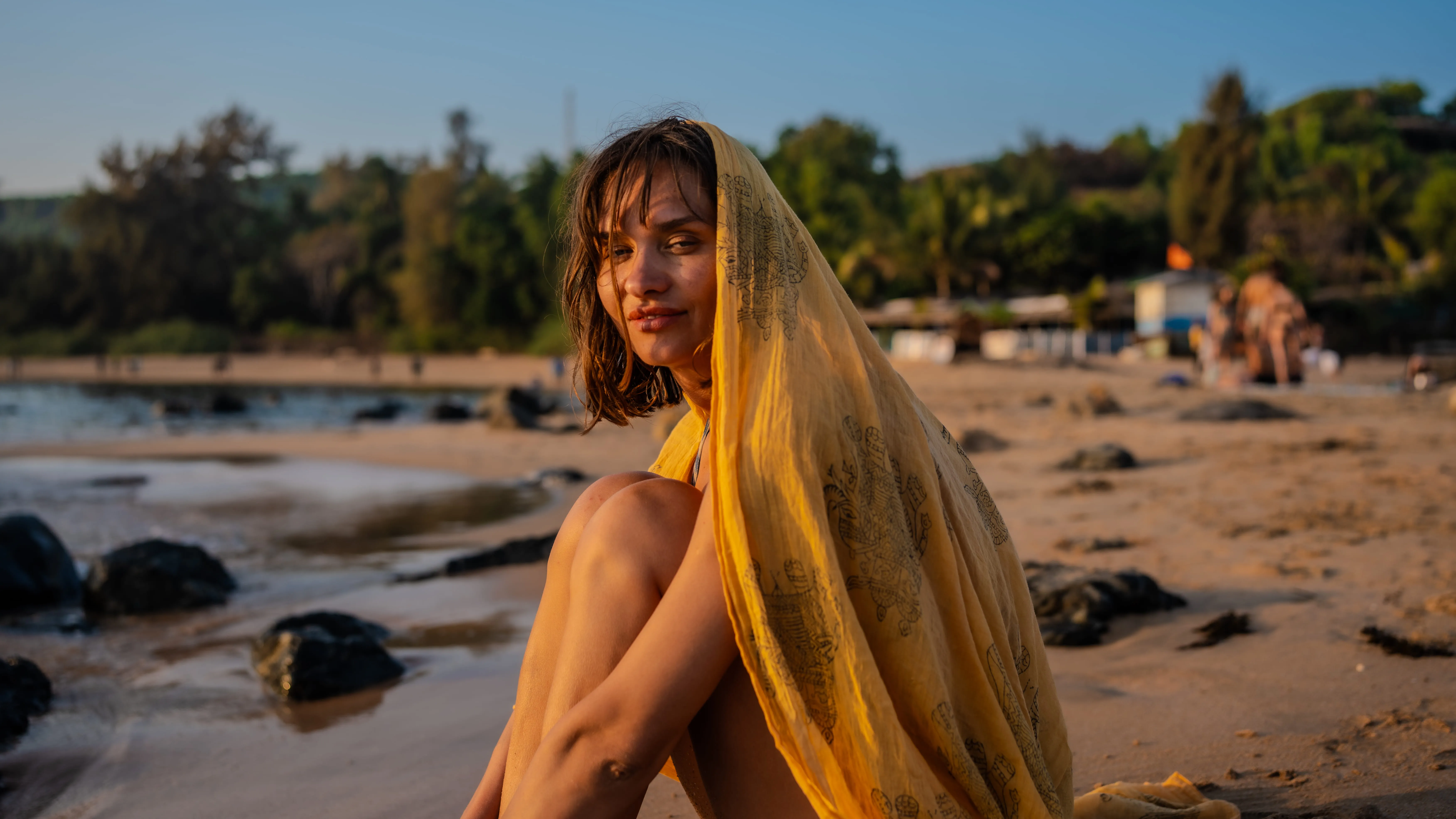 Woman draped in a yellow patterned scarf near the waterline on a Goa beach.