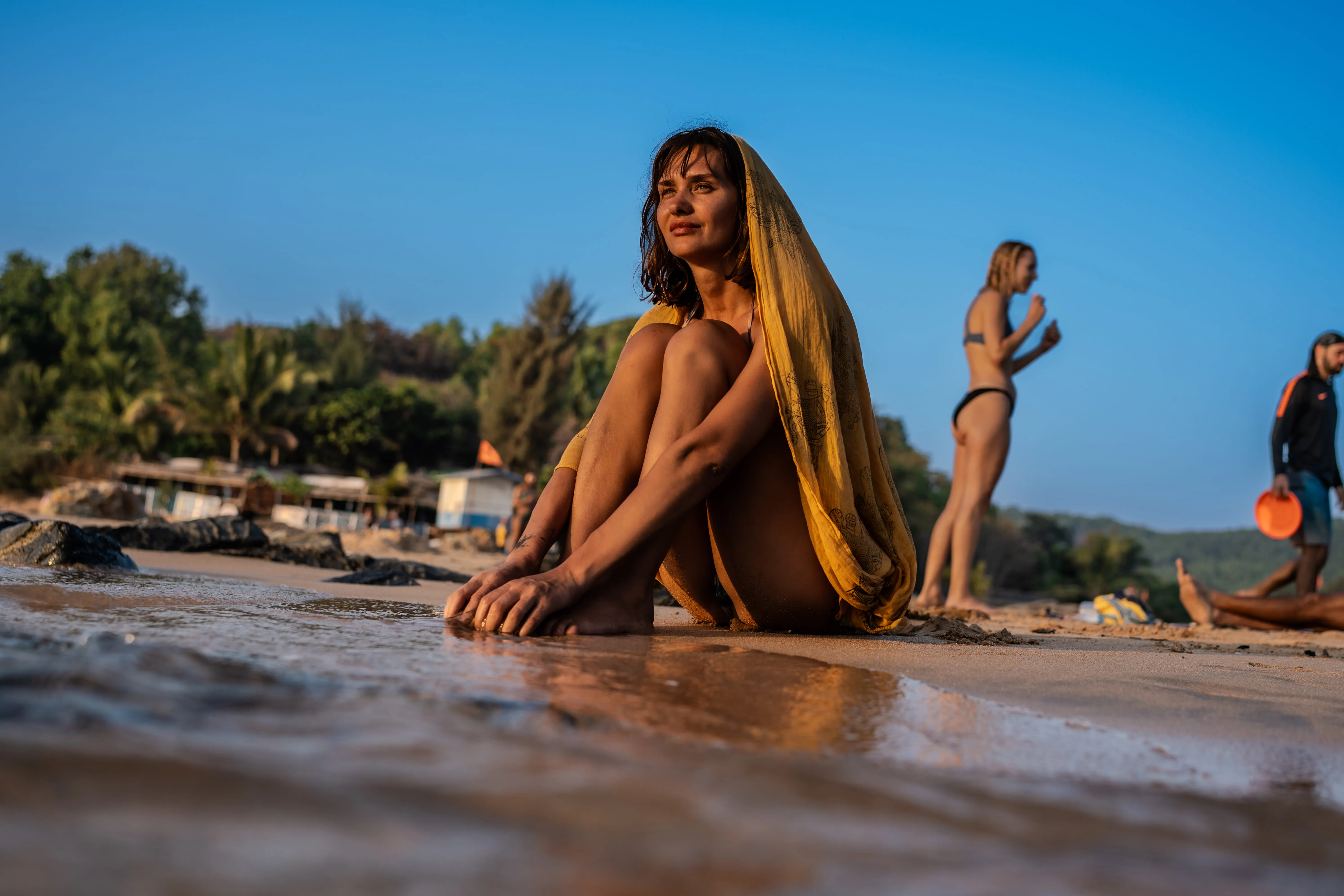 Woman in yellow patterned fabric at the water's edge on a Goa beach.