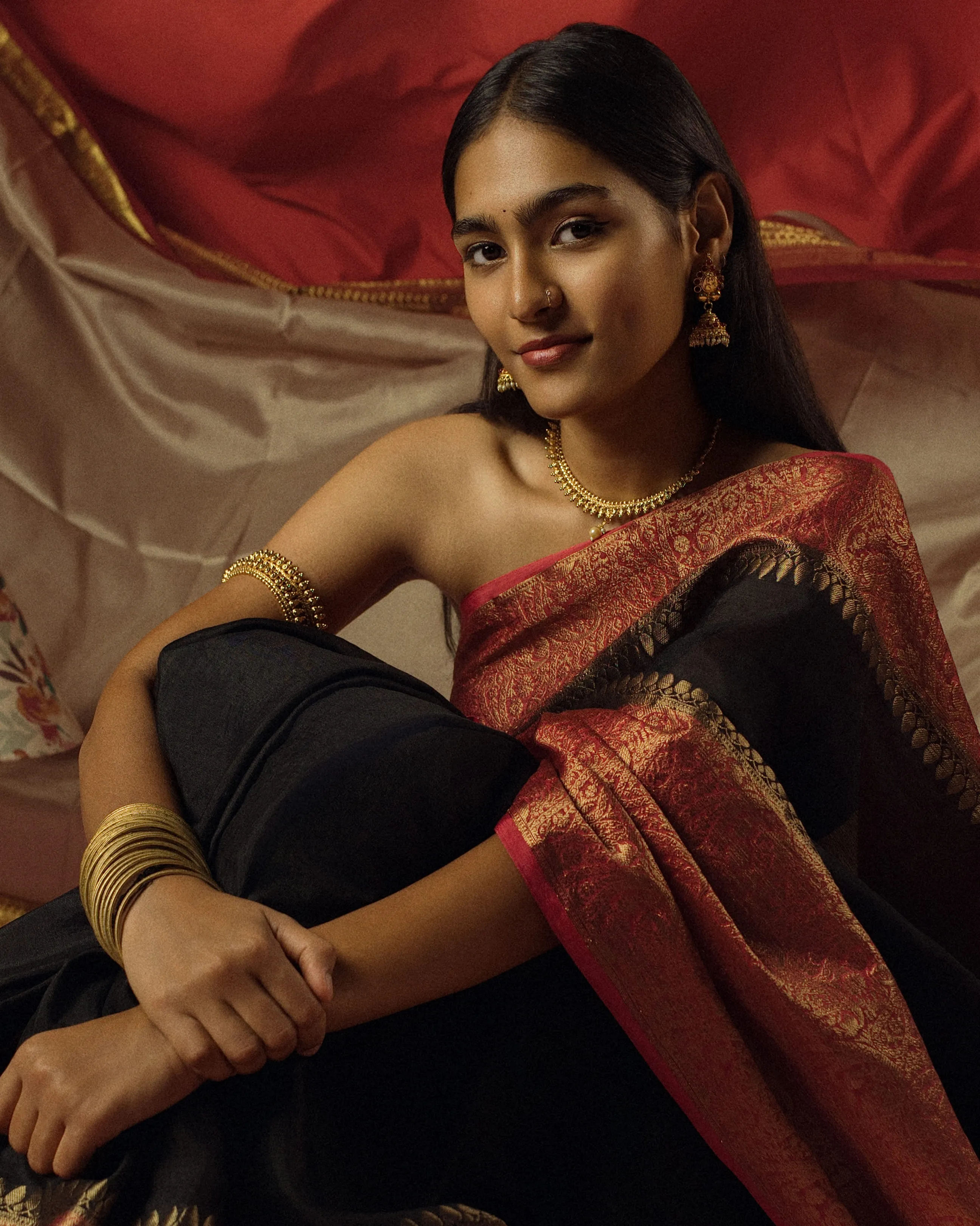 Close seated portrait of a woman in a black sari with a red and gold border.