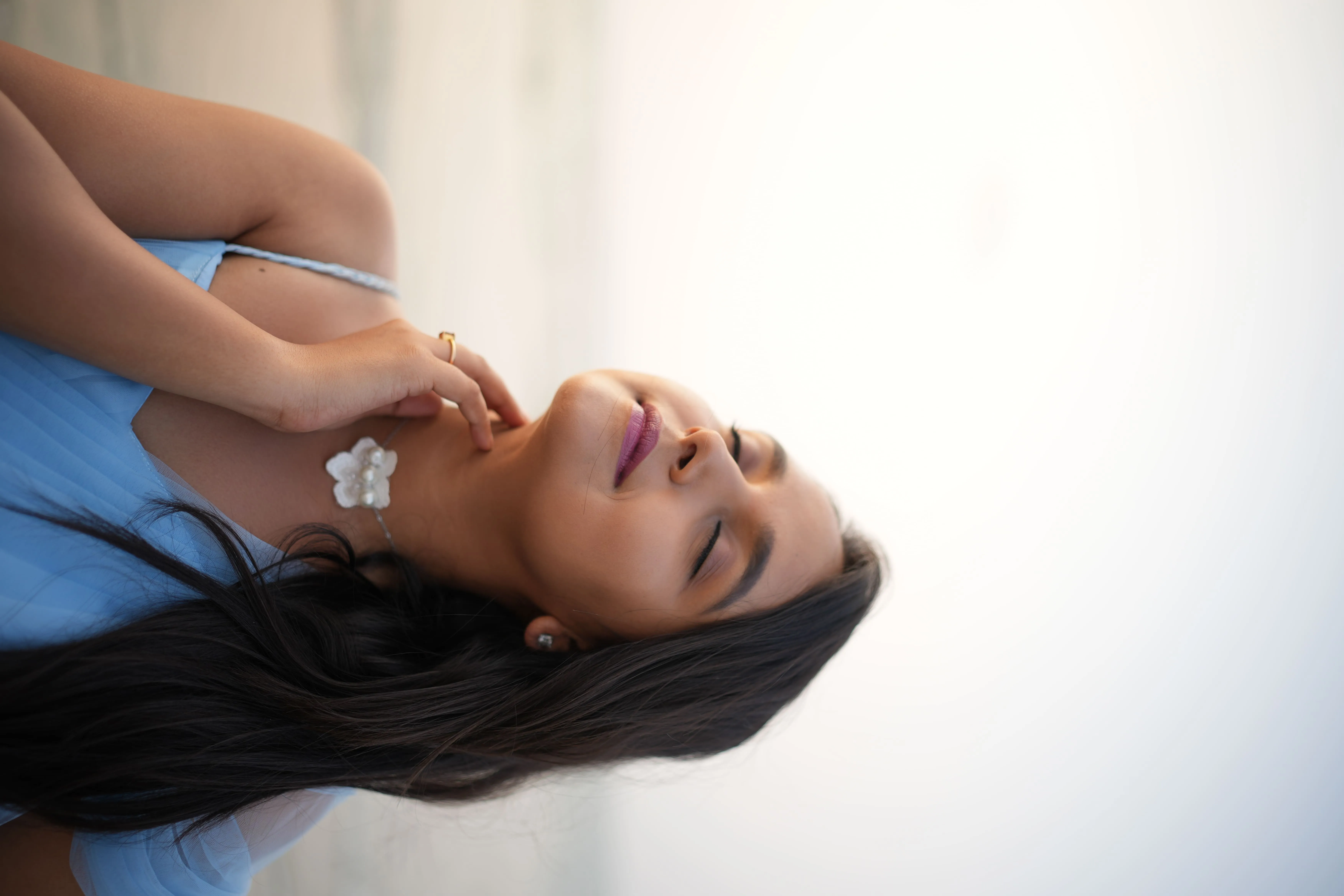 Woman in a light blue dress lying sideways in a bright contemporary portrait.