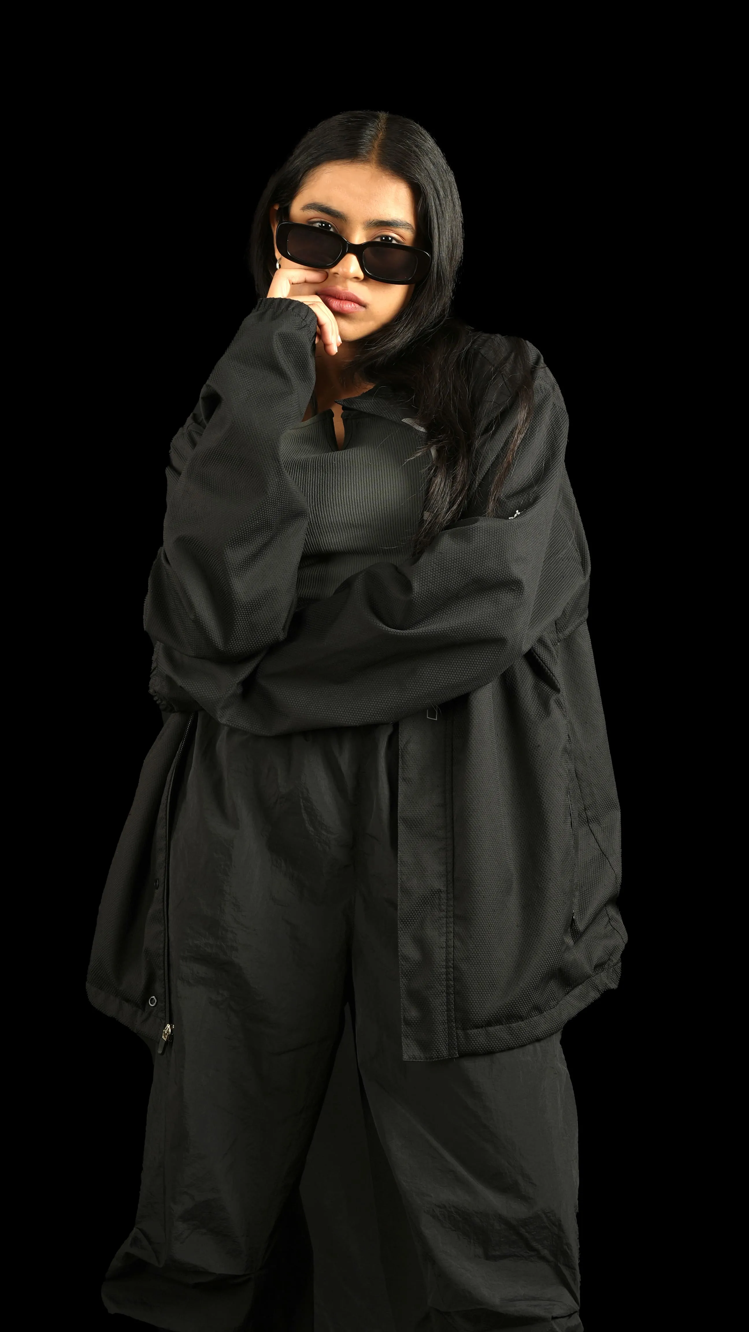 Woman in black sunglasses and a black jacket against a black studio background.