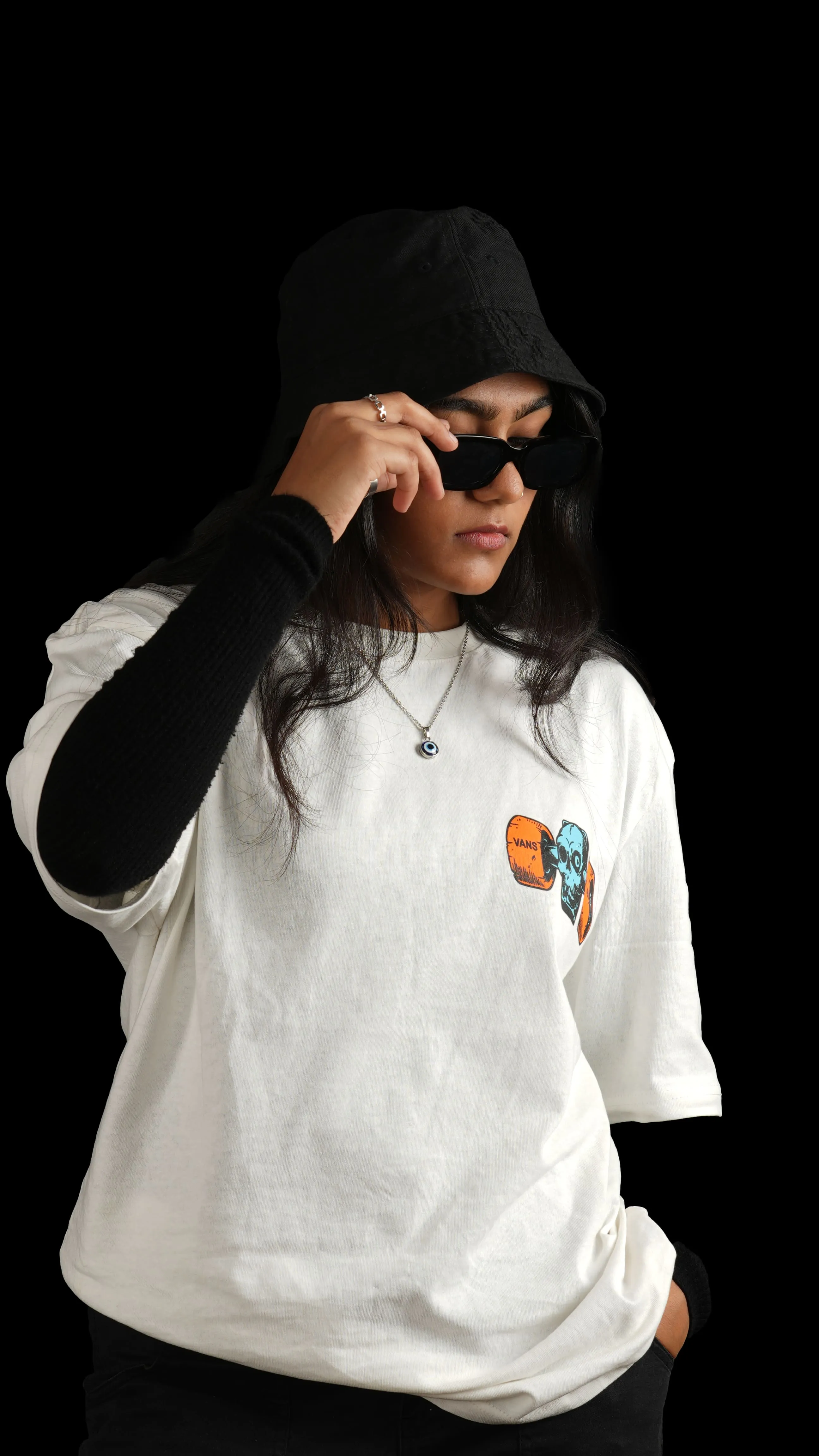 Woman in a black bucket hat and sunglasses wearing a white graphic T-shirt in a studio portrait.