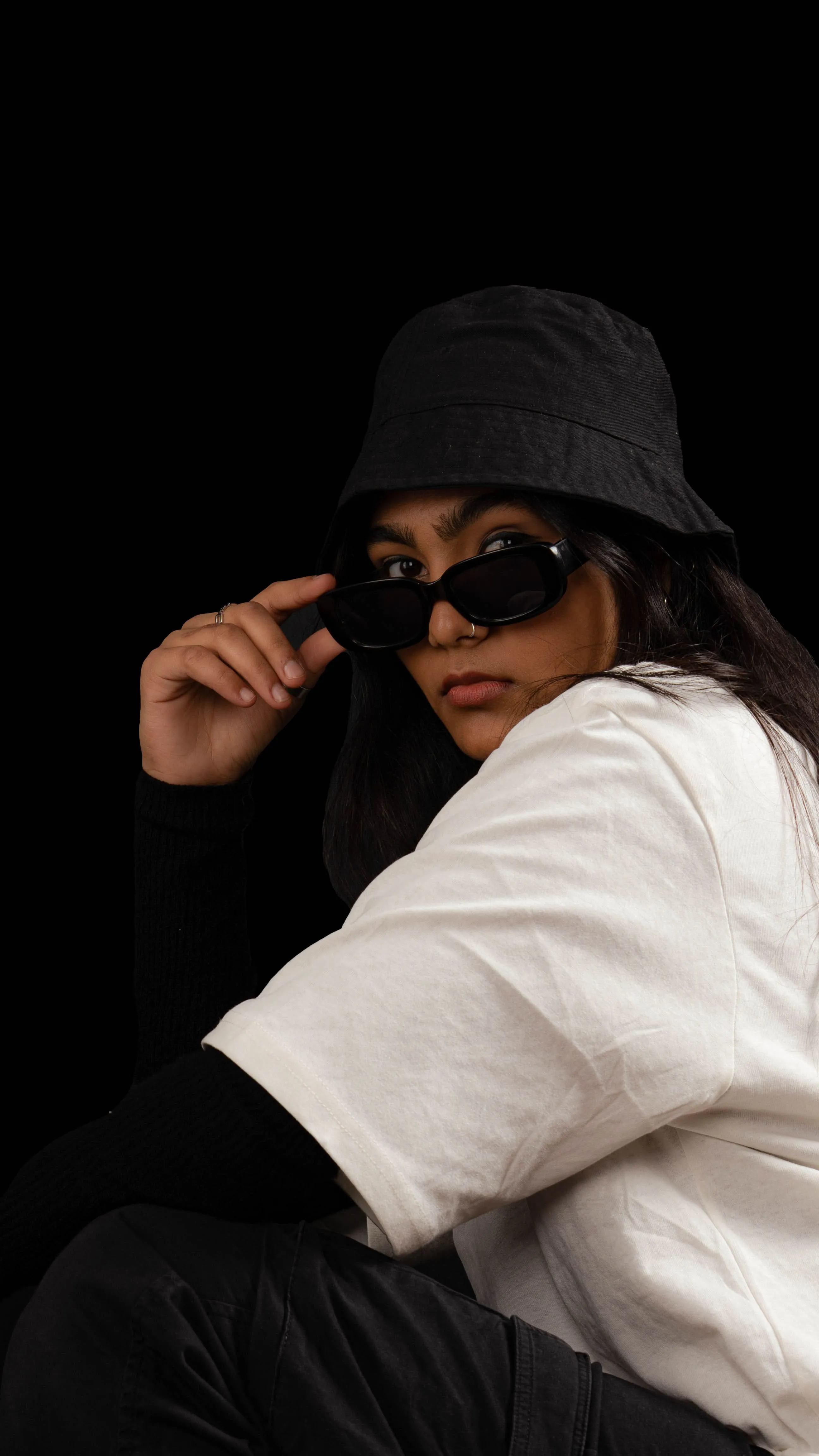 Close portrait of a woman in a black bucket hat and sunglasses against a black background.