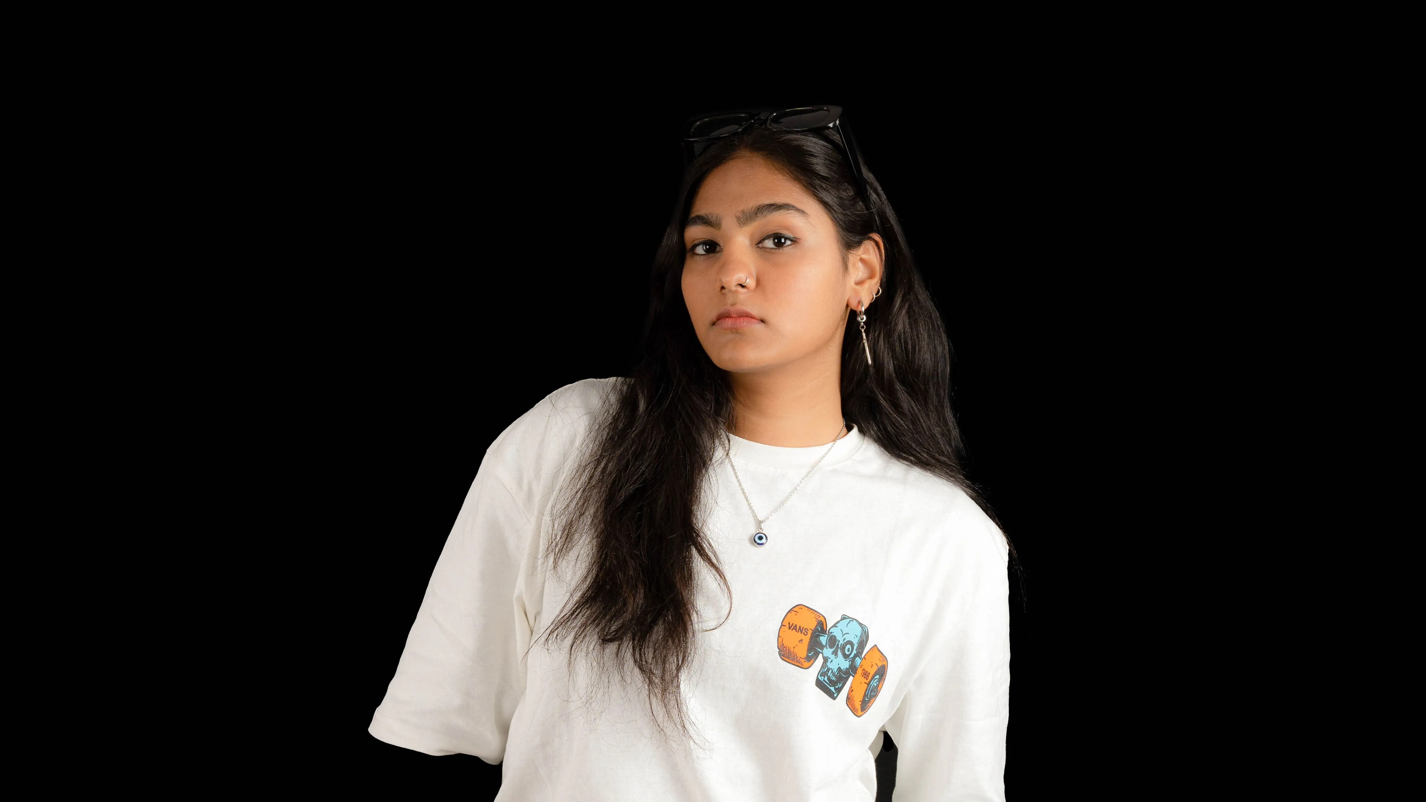 Woman in a white graphic T-shirt with sunglasses resting on her head in a studio portrait.