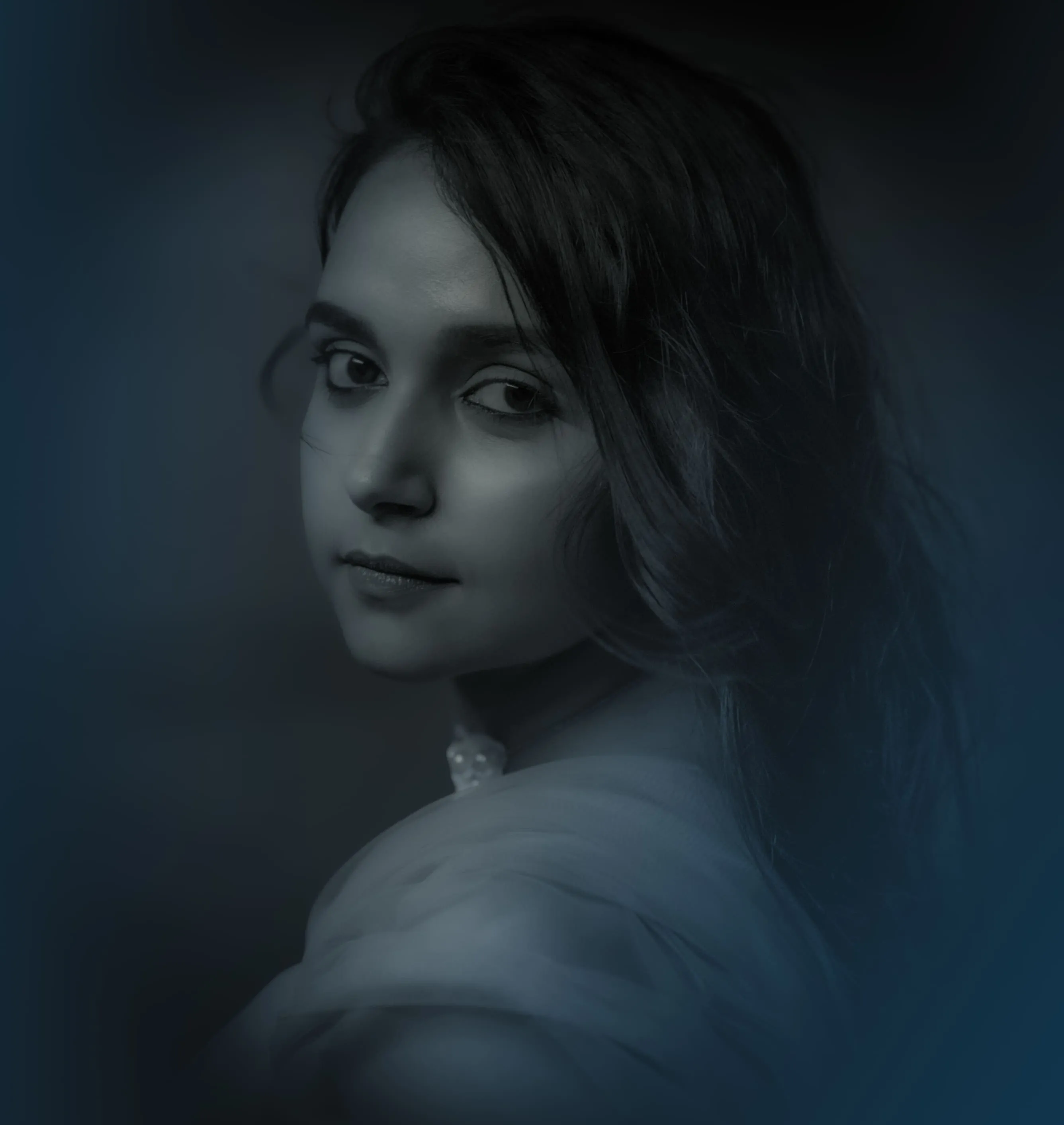 Blue-toned close portrait of a woman partially wrapped in pale fabric.
