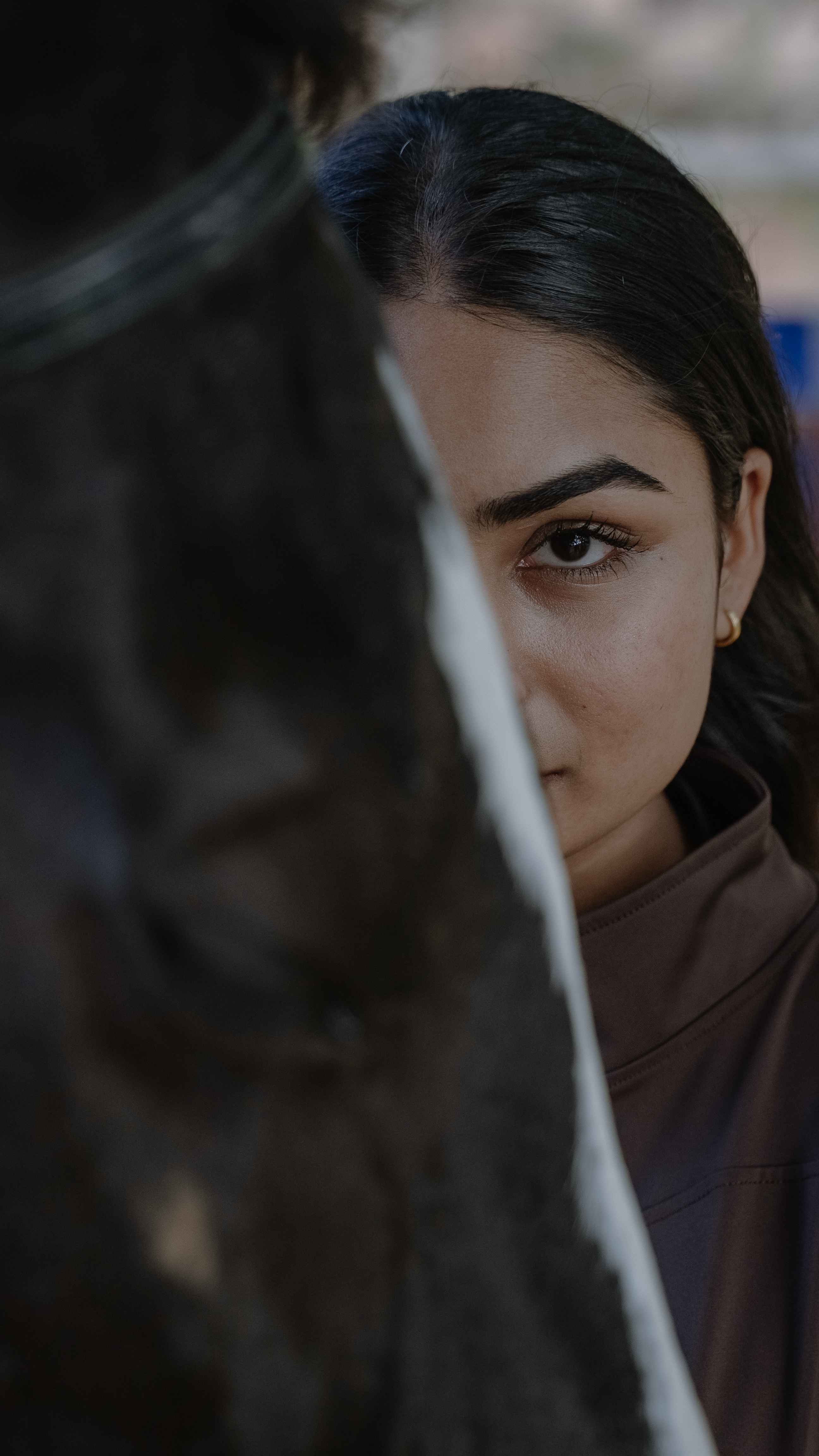 Close portrait of a woman partially concealed behind a dark foreground object.