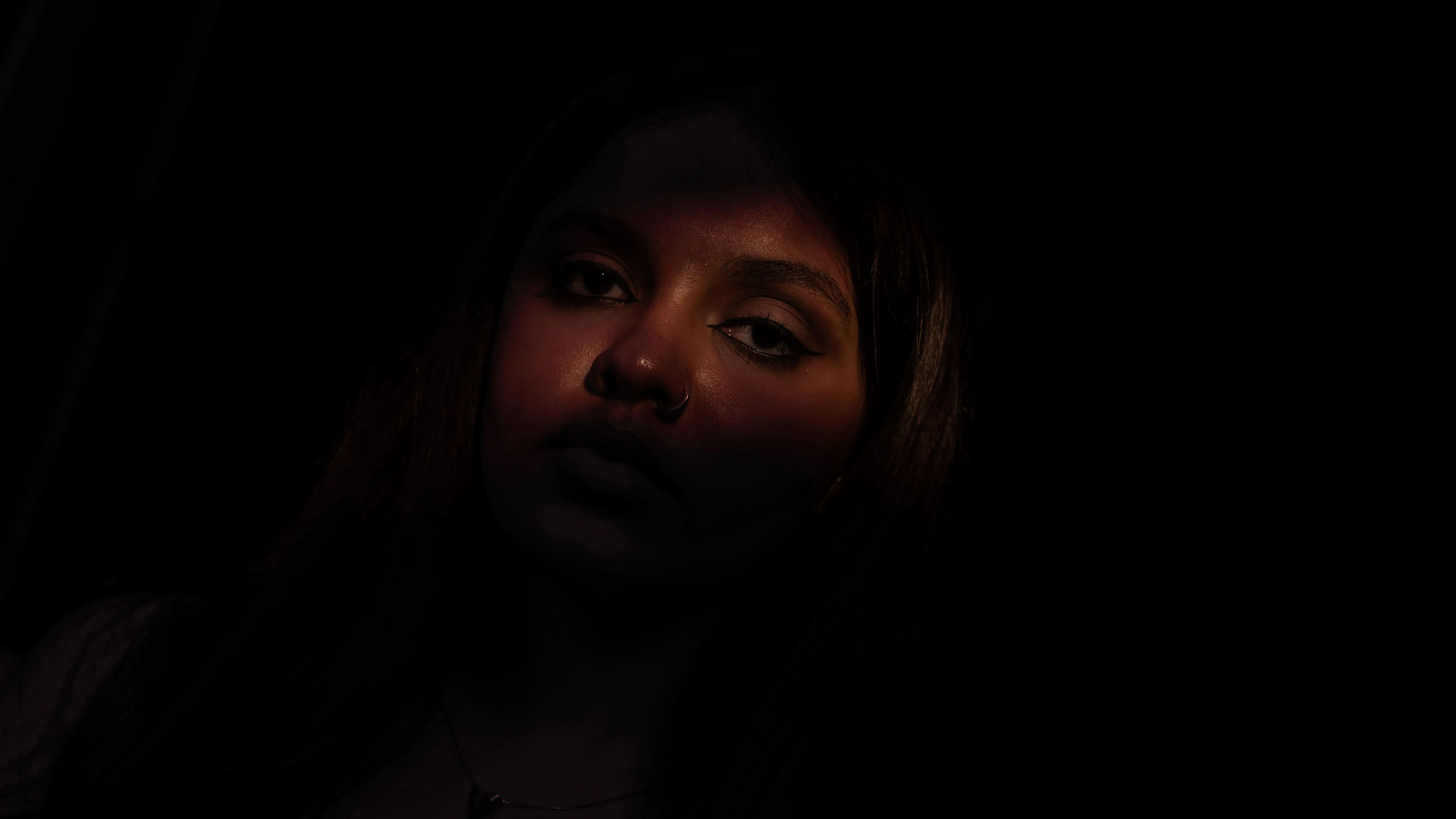 Low-lit close portrait of a woman looking toward the camera.