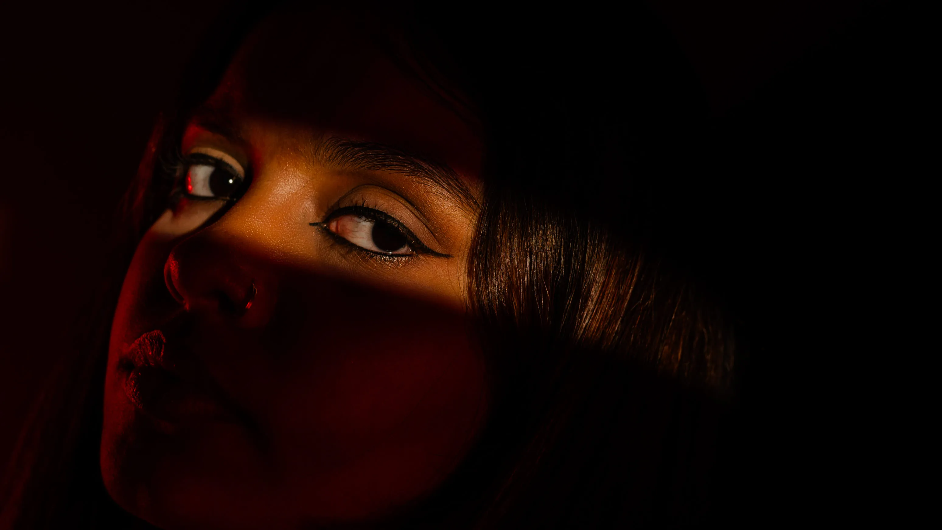 Low-lit close portrait of a woman illuminated by red light.