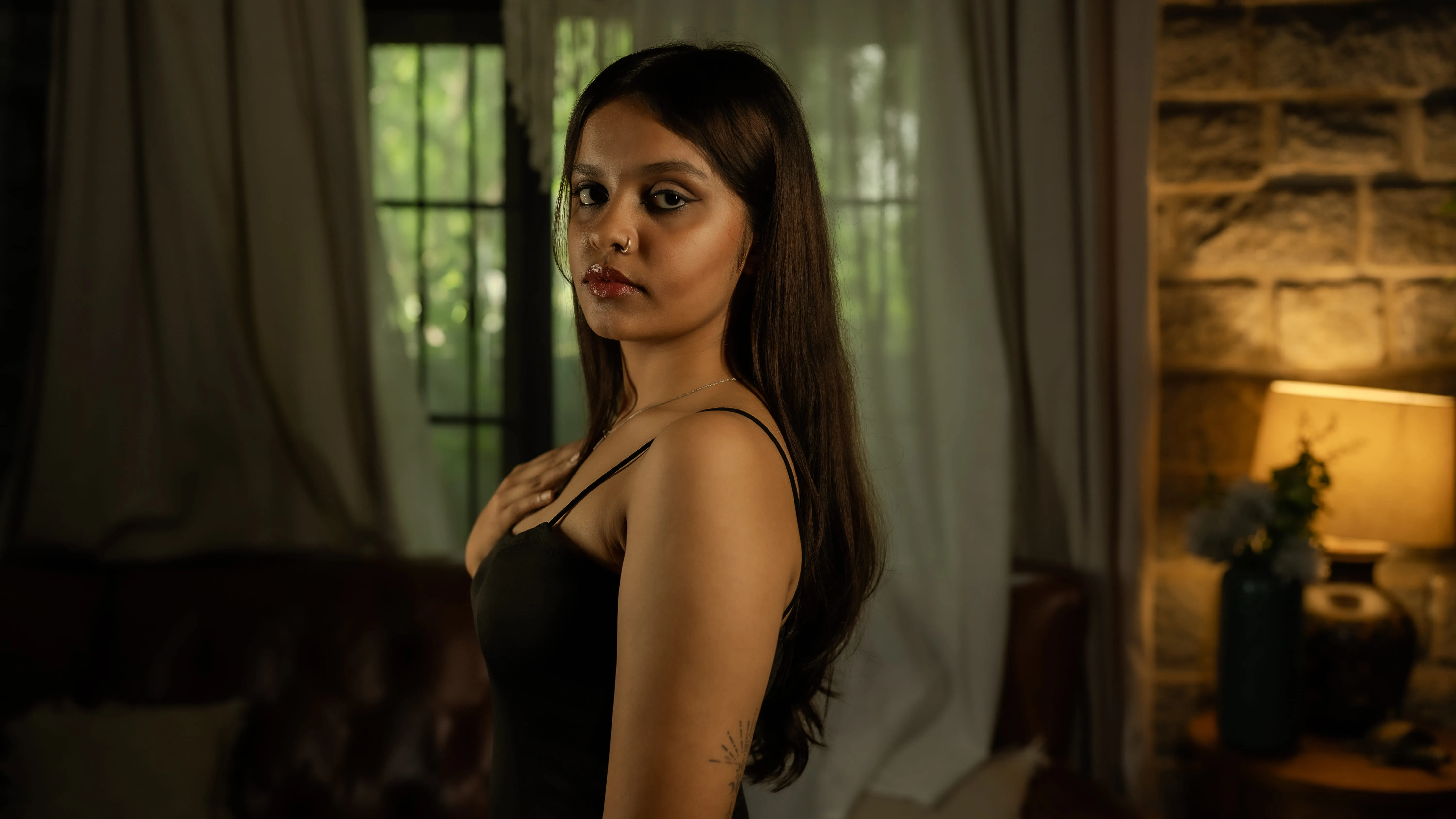 Woman in a black sleeveless dress in a warmly lit interior.