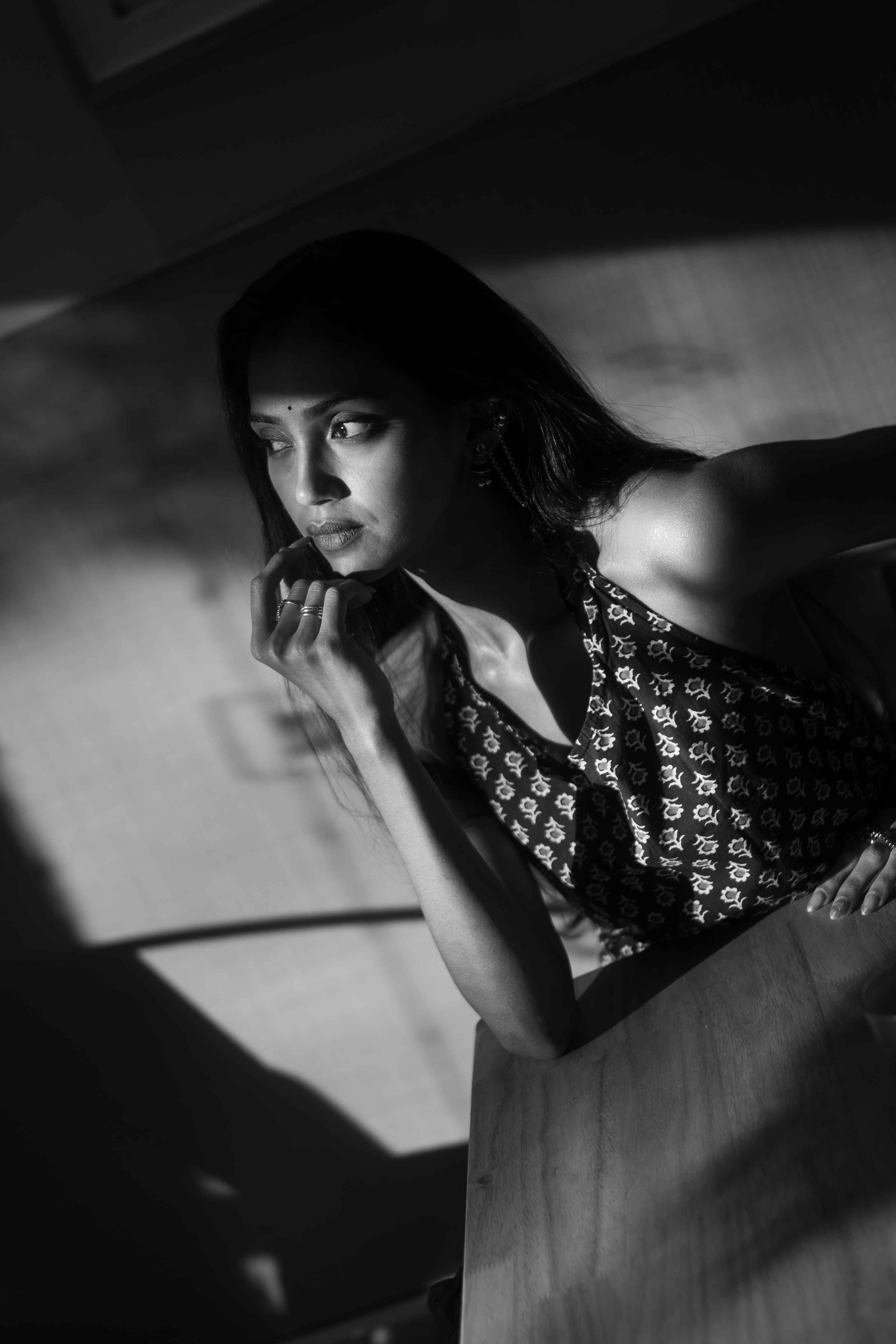 Black-and-white portrait of a woman in a patterned sleeveless top at a wooden table.