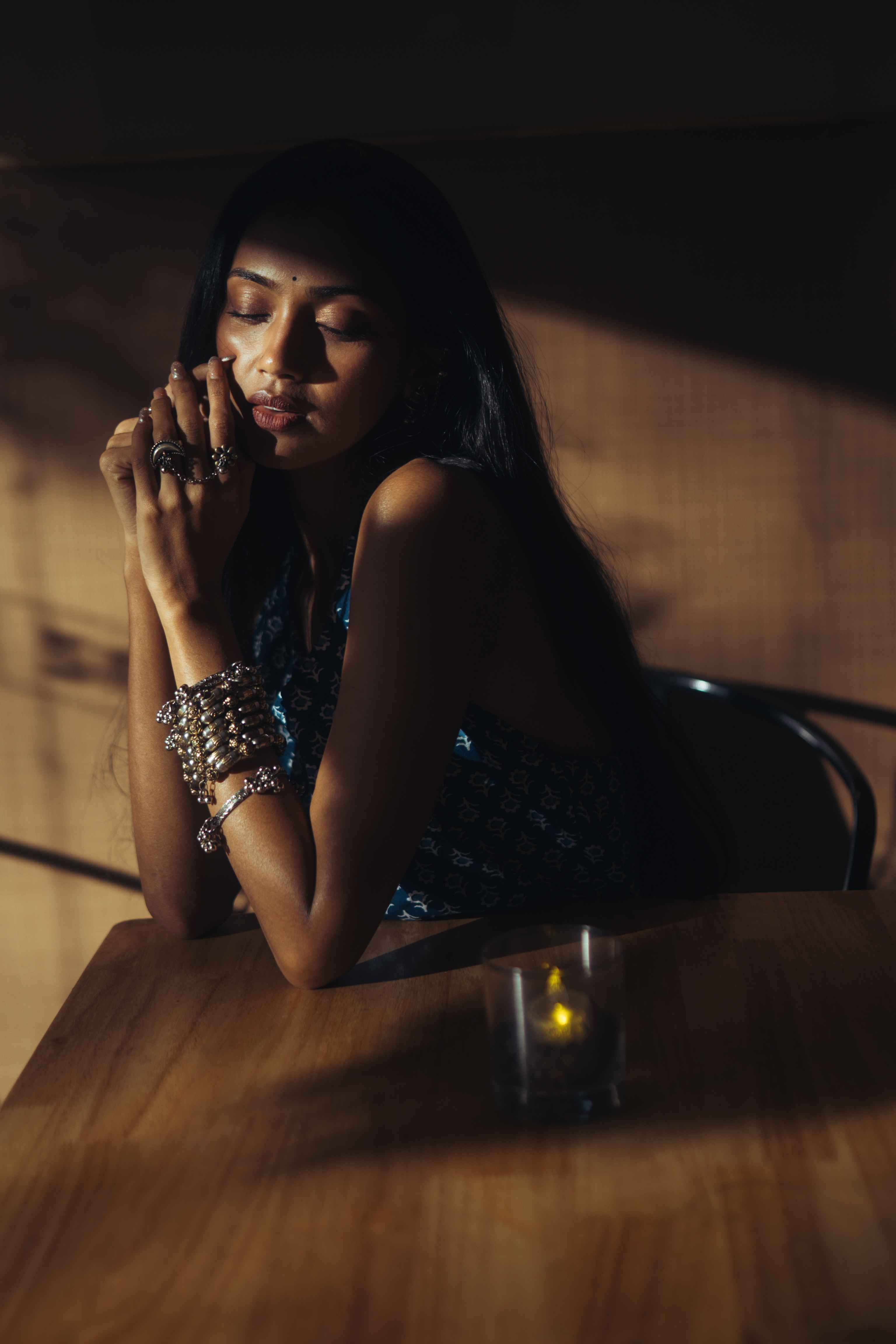 Woman resting her face on her hands at a wooden table in warm light.