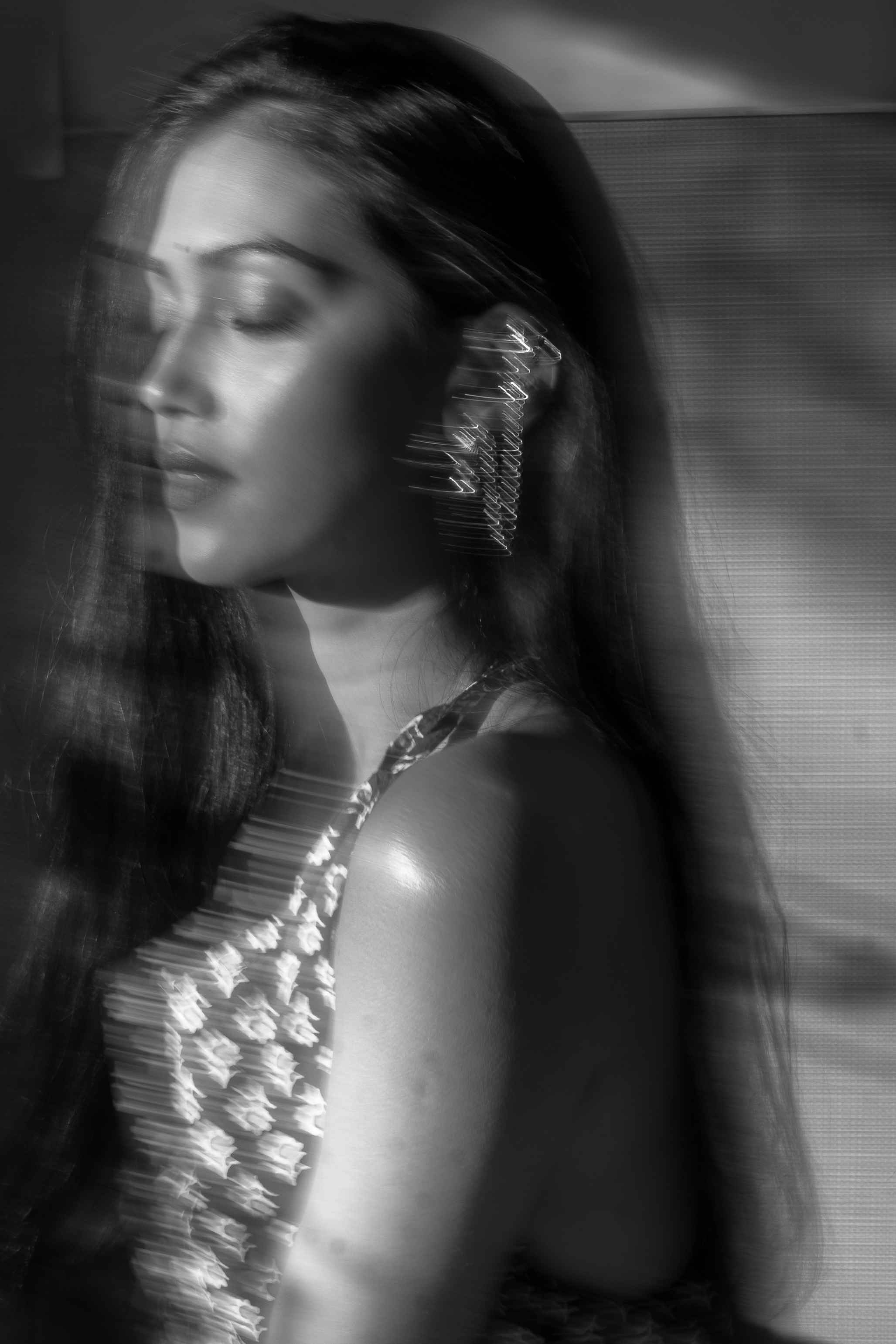 Black-and-white close portrait of a woman with her eyes closed and hands beside her face.