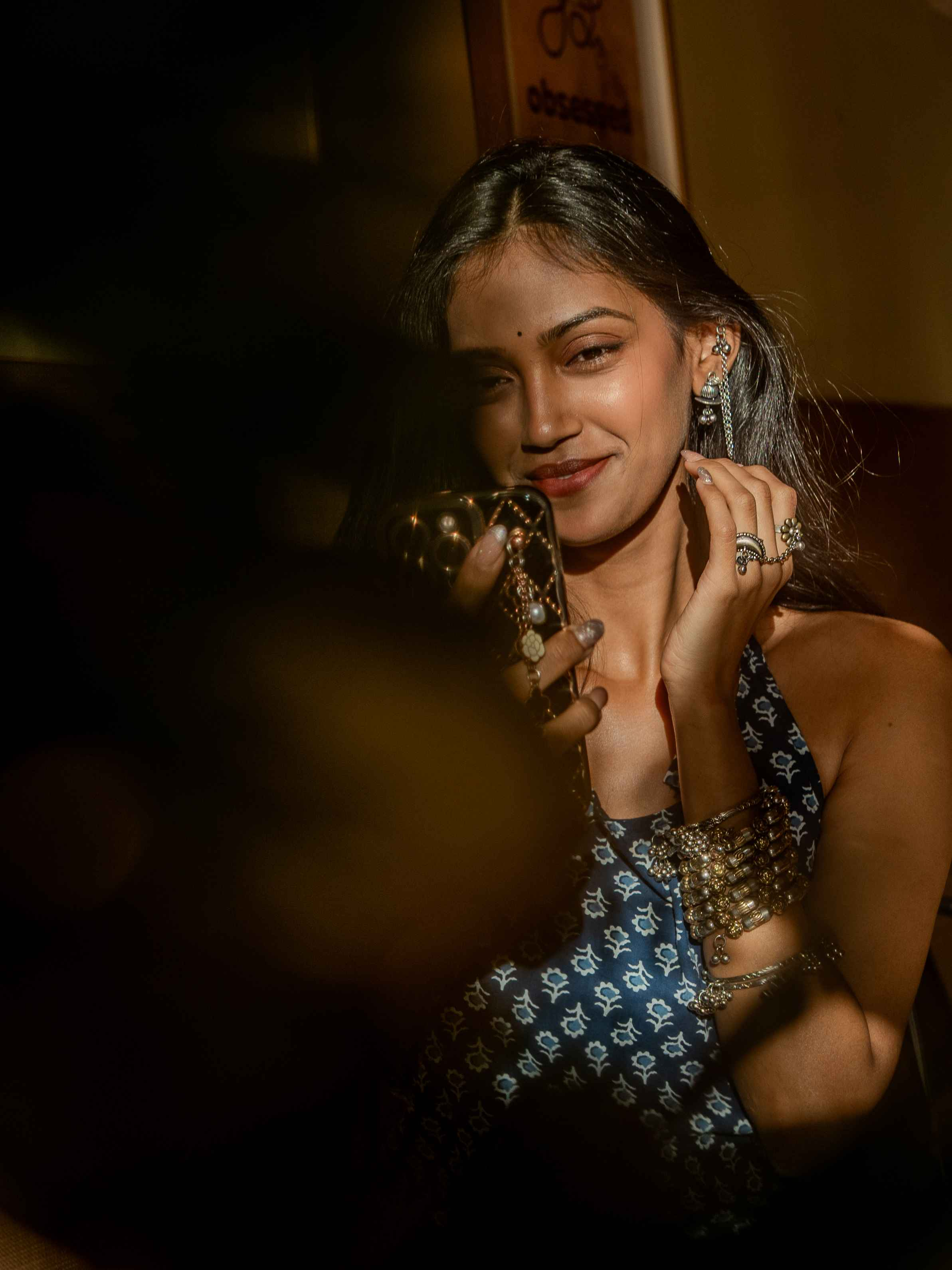 Woman in a dark blue patterned top with layered jewellery in a warm close portrait.