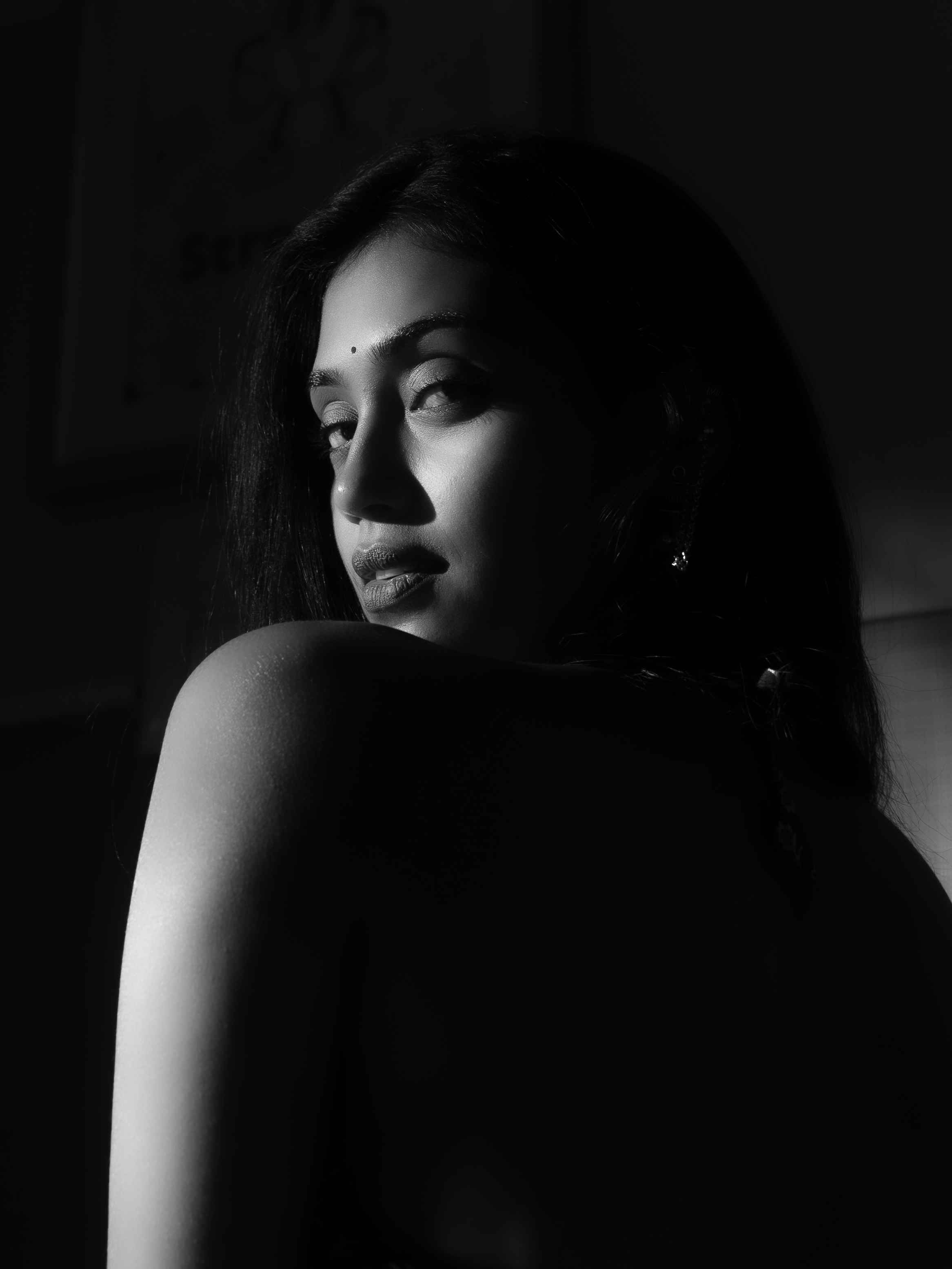 Woman touching her earring beside a smartphone in a warm reflected portrait.