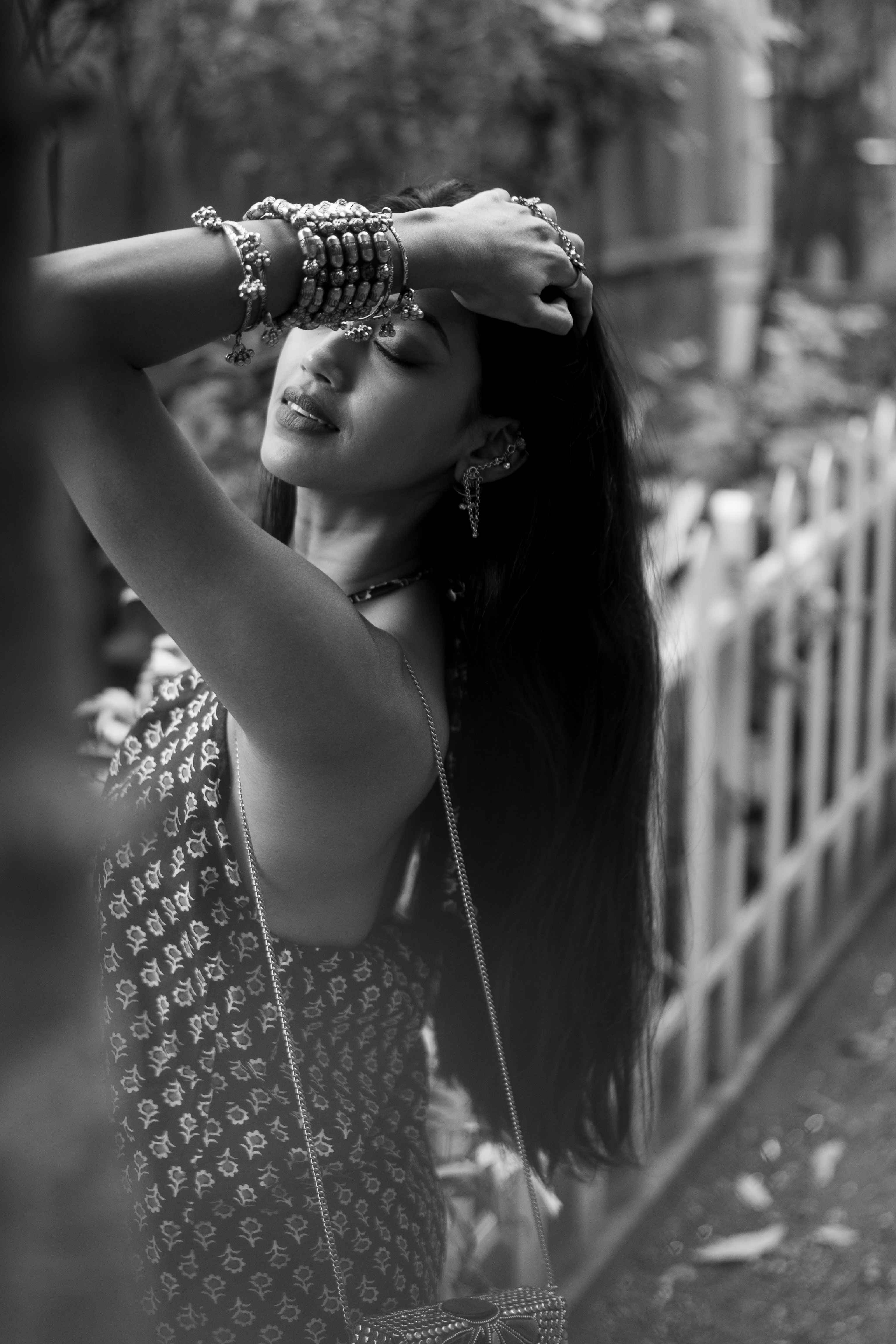 Black-and-white outdoor portrait of a woman raising her arms across her forehead.