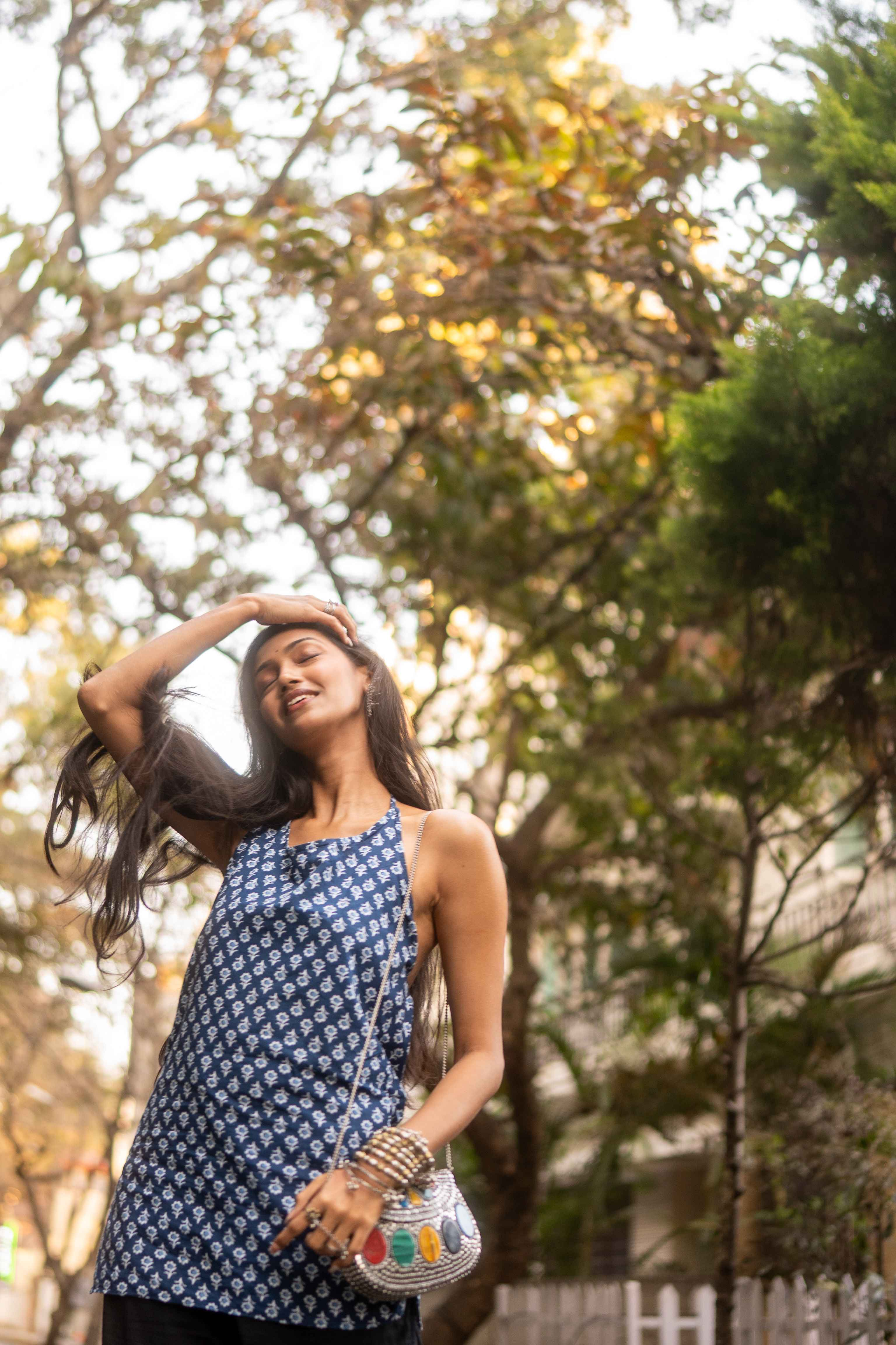 Sunlit outdoor portrait of a smiling woman in a blue patterned halter top with her eyes closed.