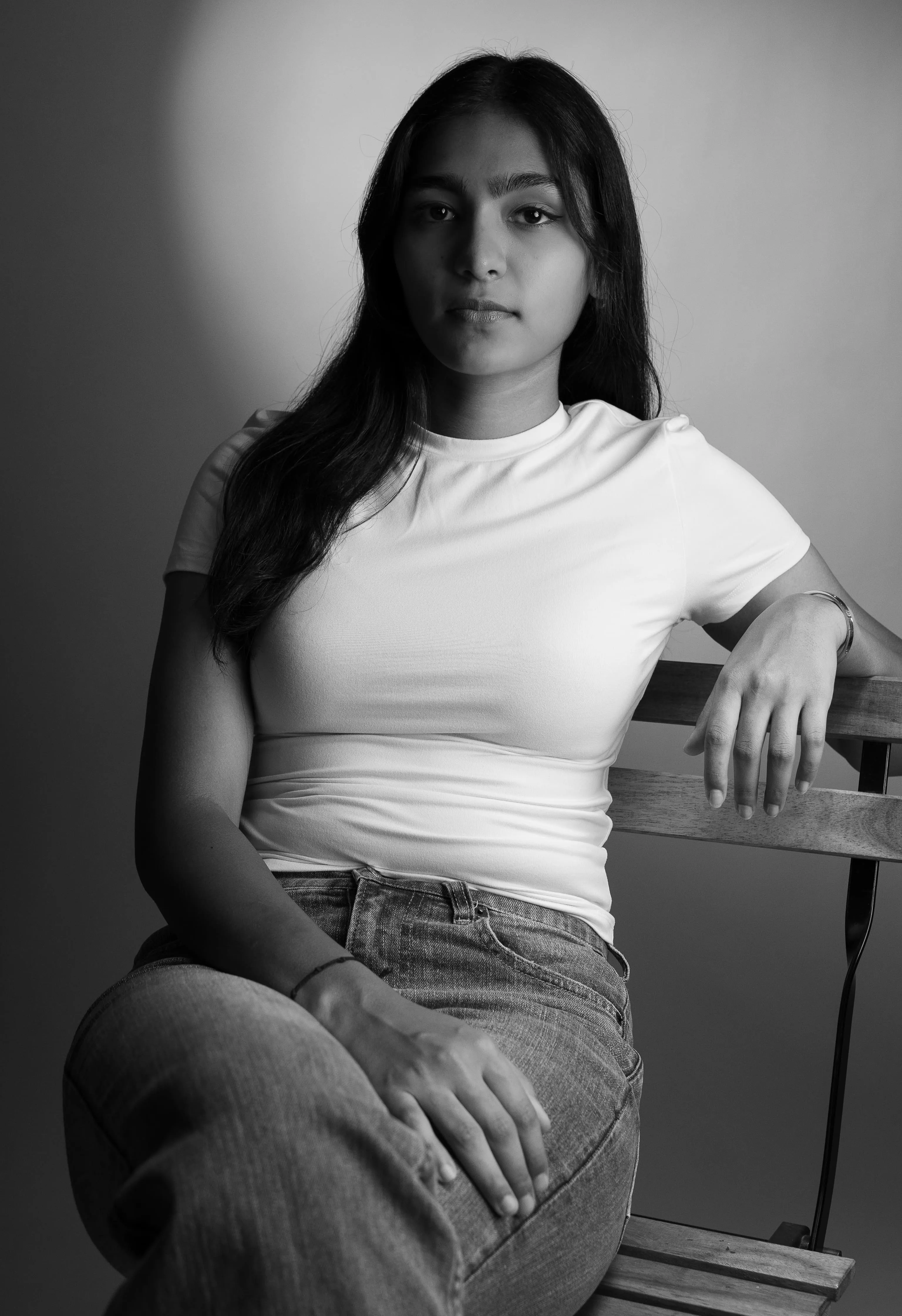 Black-and-white portrait of a woman in a white T-shirt and jeans seated on a wooden chair.