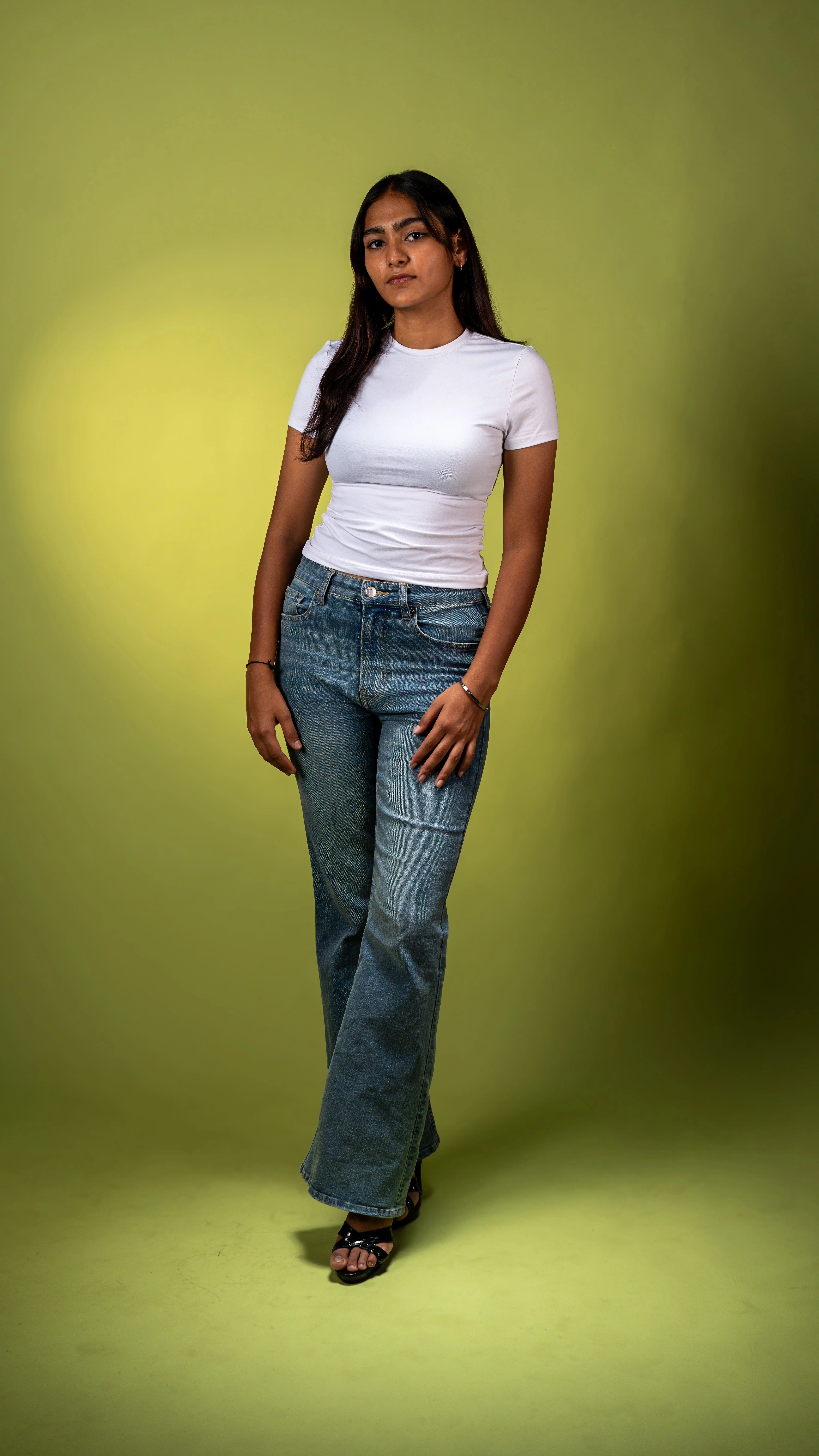 Full-length portrait of a woman in a white T-shirt and blue jeans against a yellow-green background.