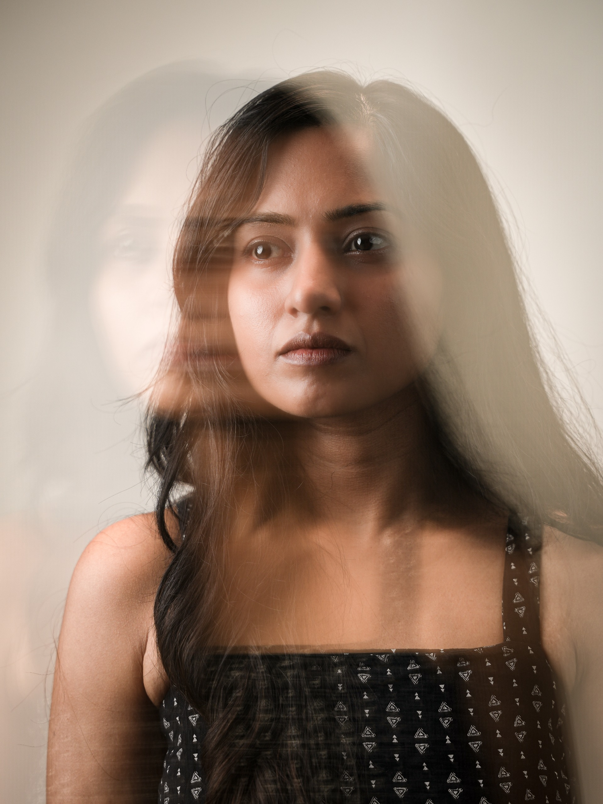 Soft reflected close portrait of a woman in a dark patterned sleeveless top.