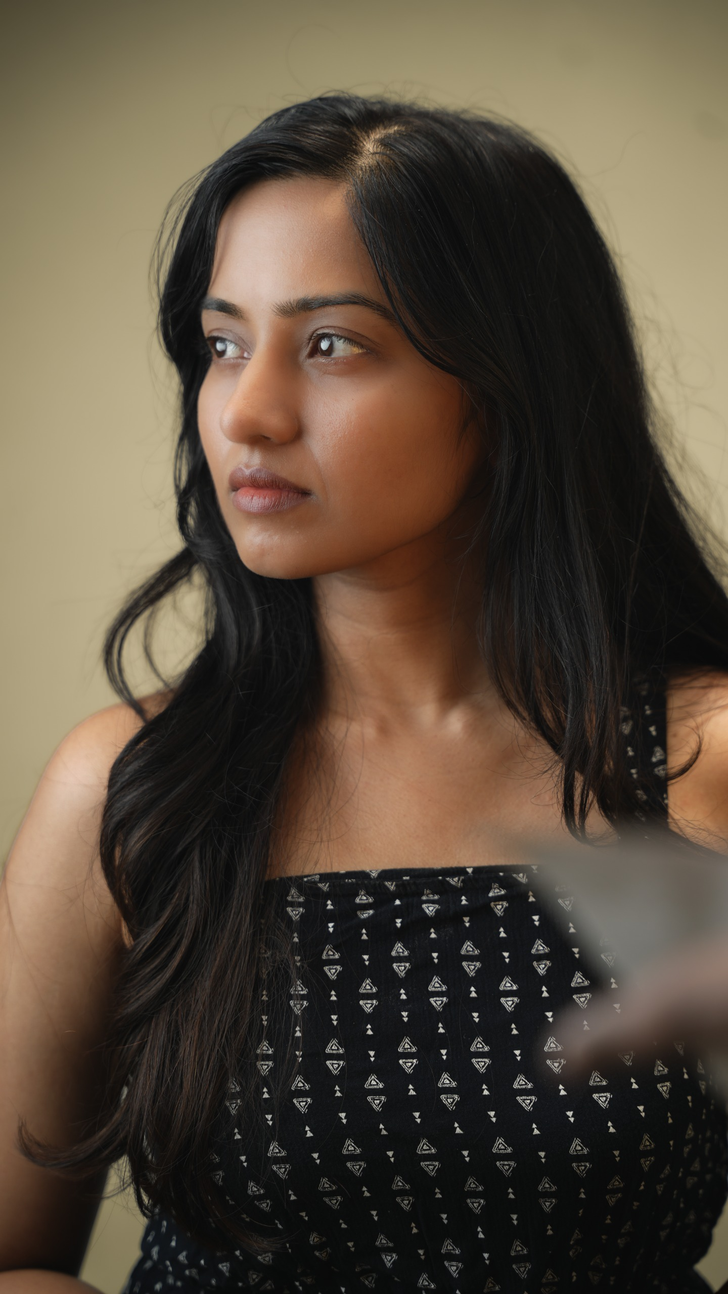 Woman in a dark patterned sleeveless top looking to the side in a soft portrait.