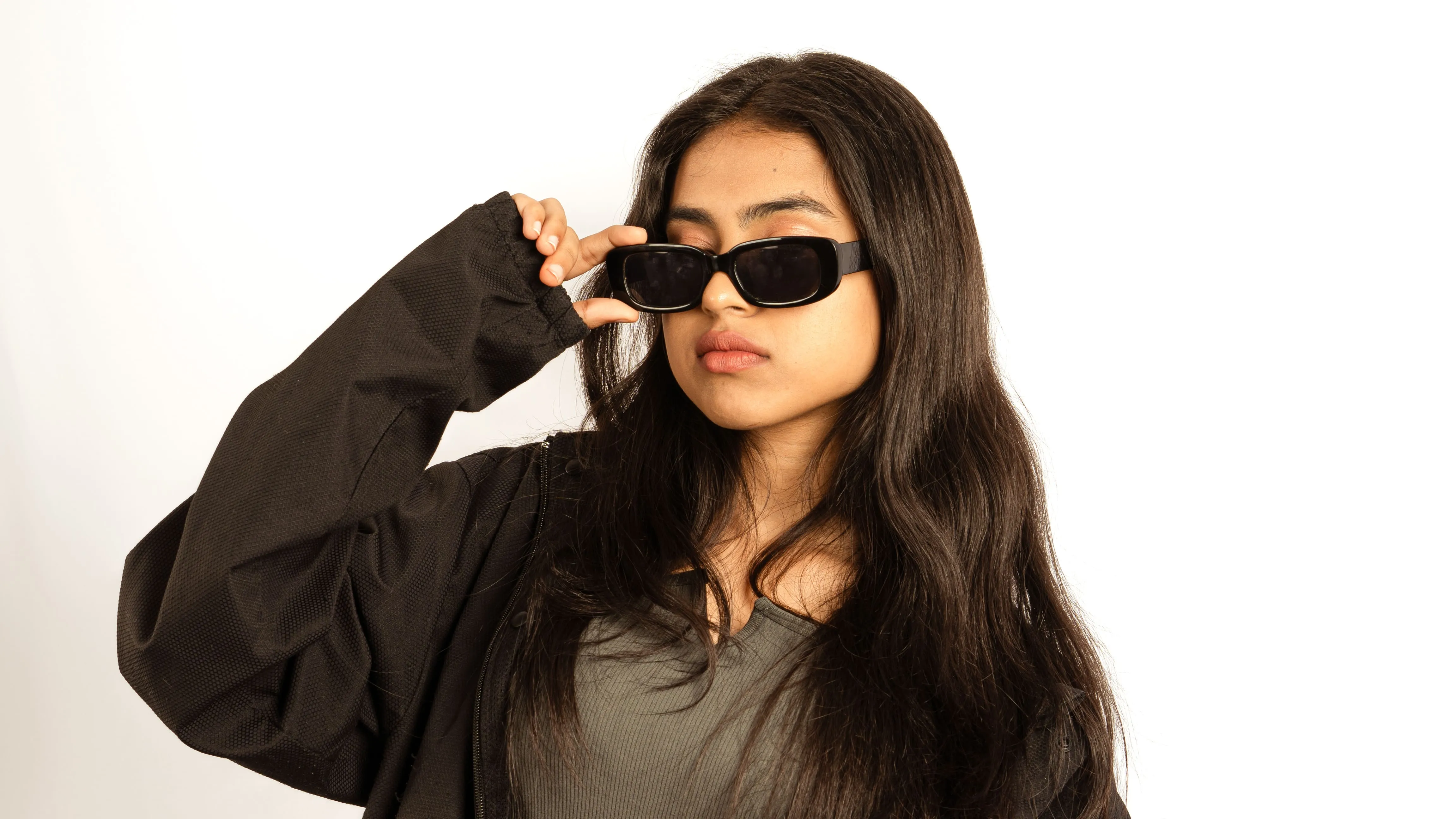 Woman adjusting black sunglasses in a contemporary studio portrait.