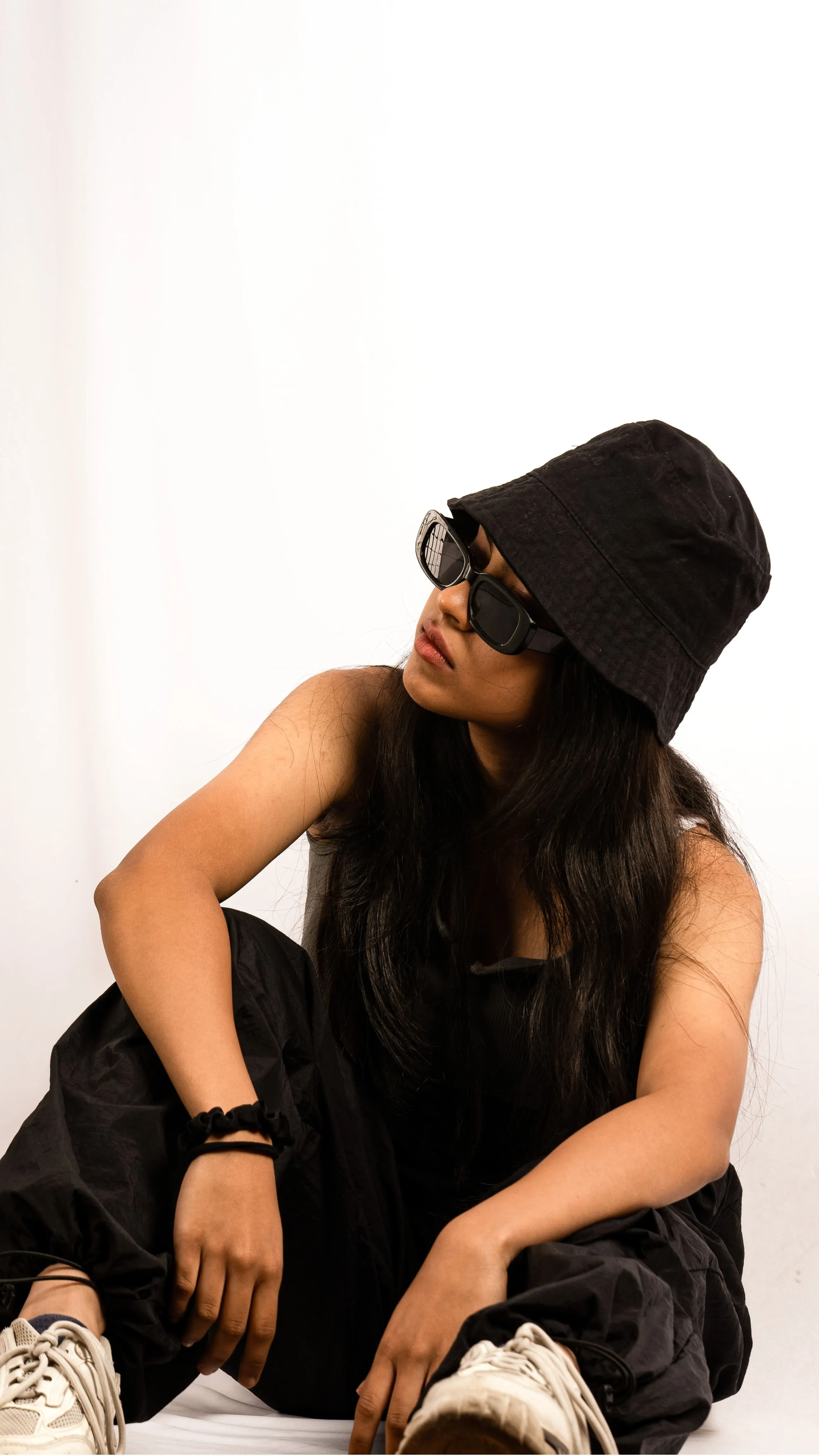 Seated woman in a black bucket hat and sunglasses in a studio portrait.