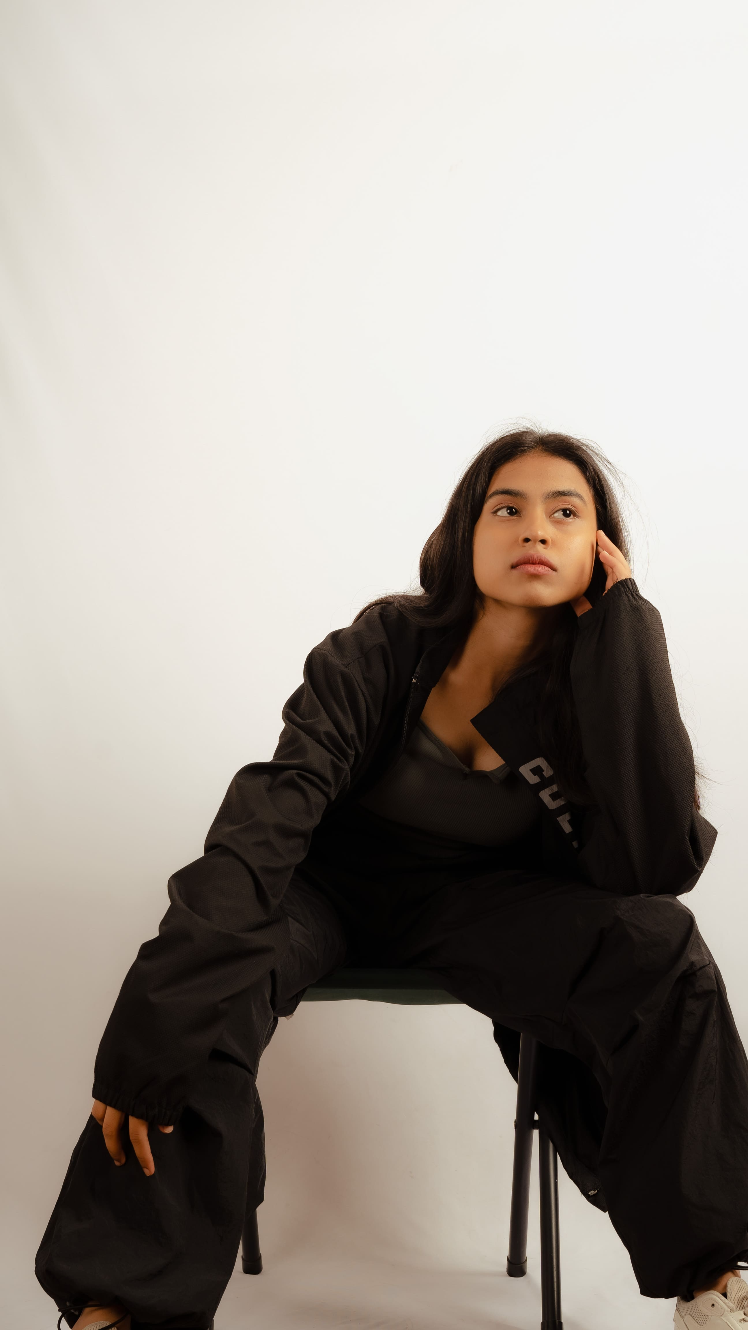 Seated woman in black clothing resting her head on one hand in a studio portrait.