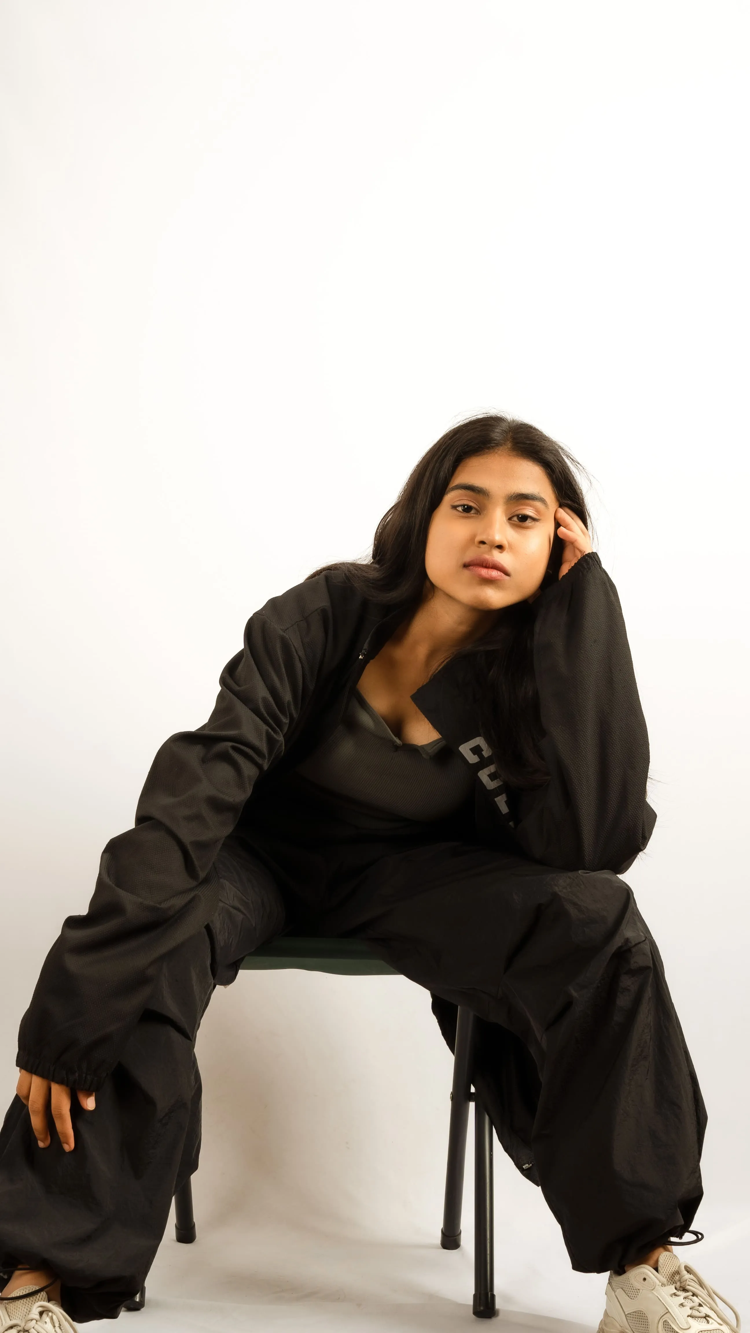 Seated woman in black clothing resting her head on one hand in a studio portrait.