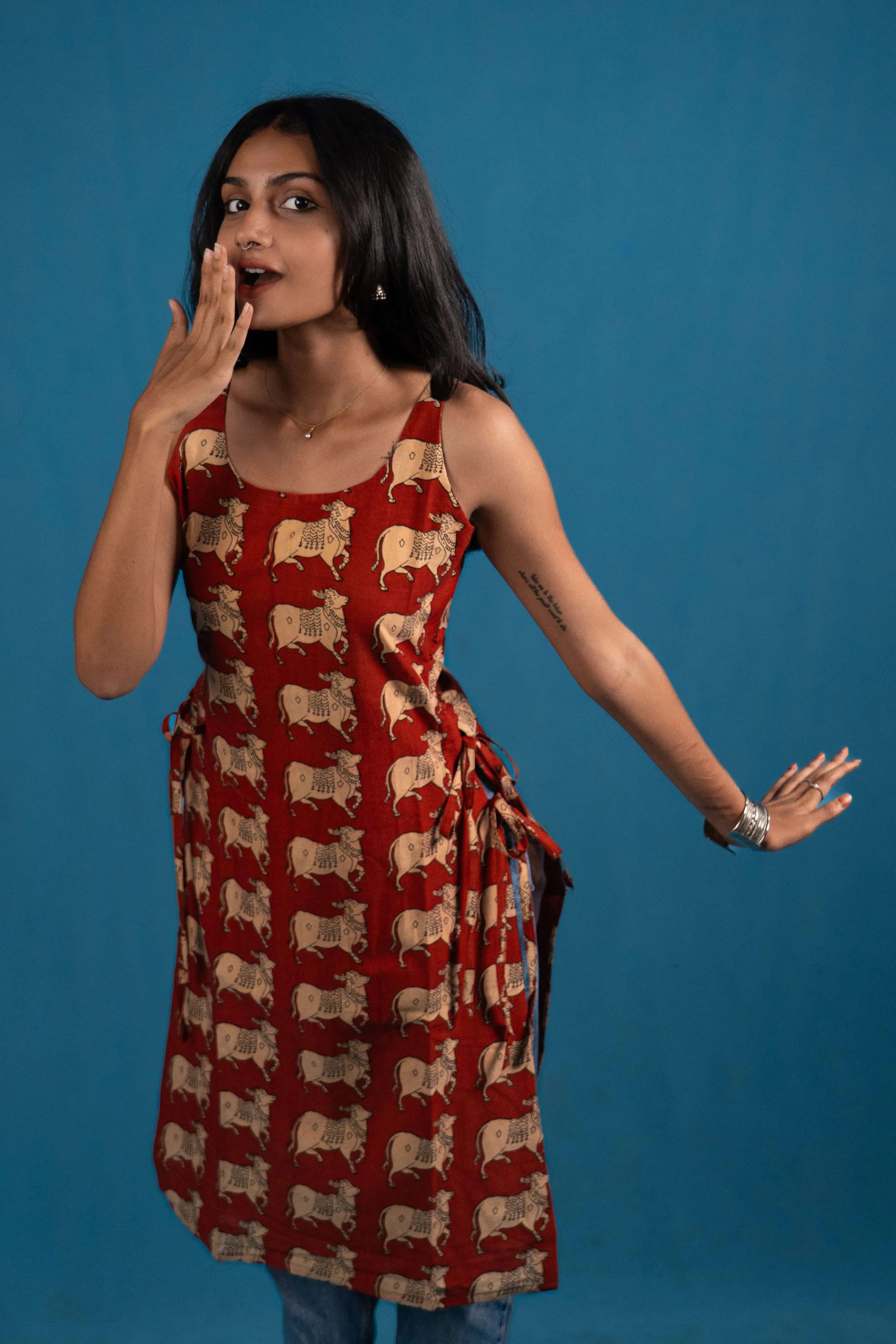 Woman in a red cow-print sleeveless top with one hand near her mouth for Indyvarna.