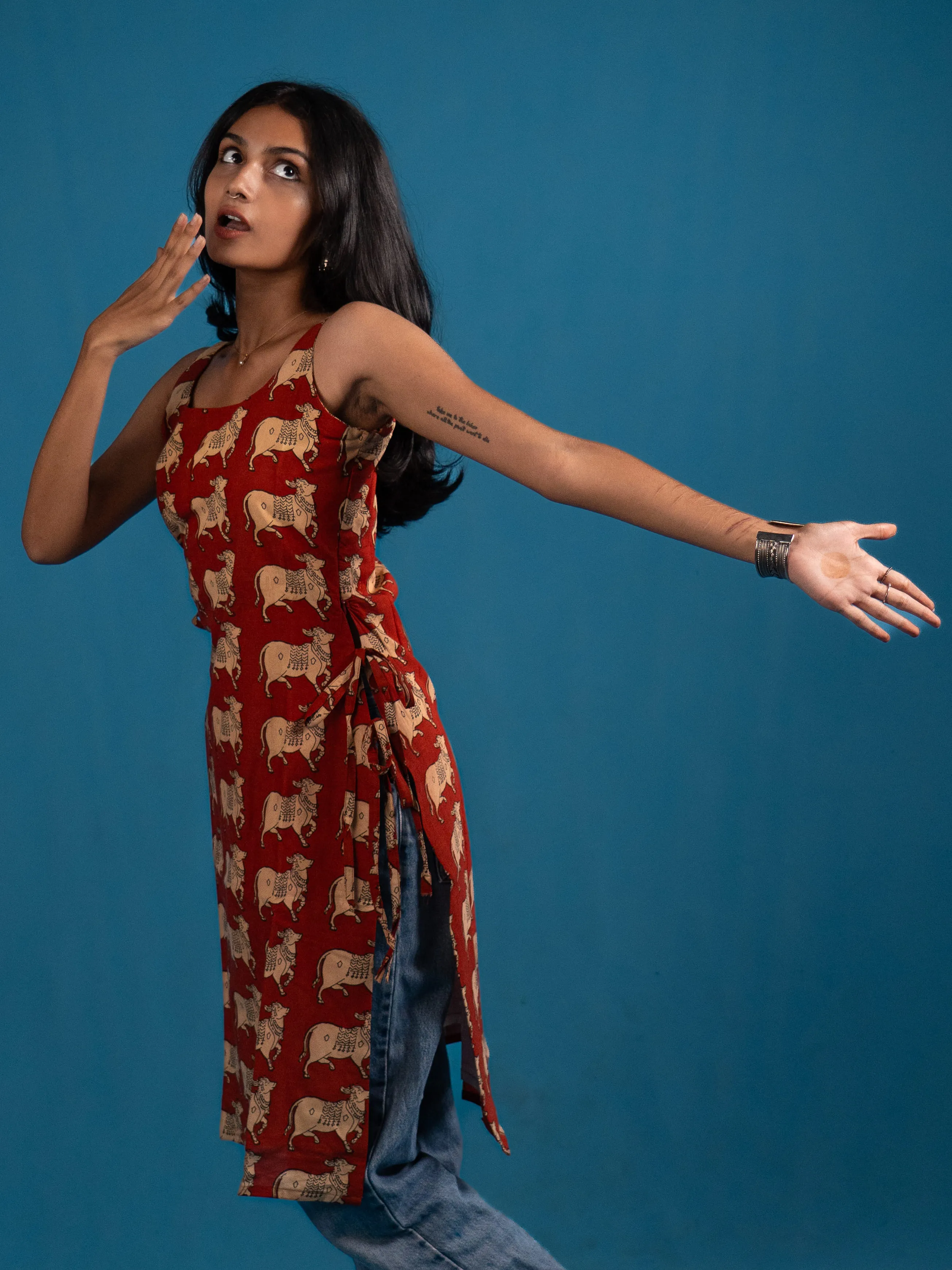 Woman in a red cow-print sleeveless top with both arms extended for Indyvarna.