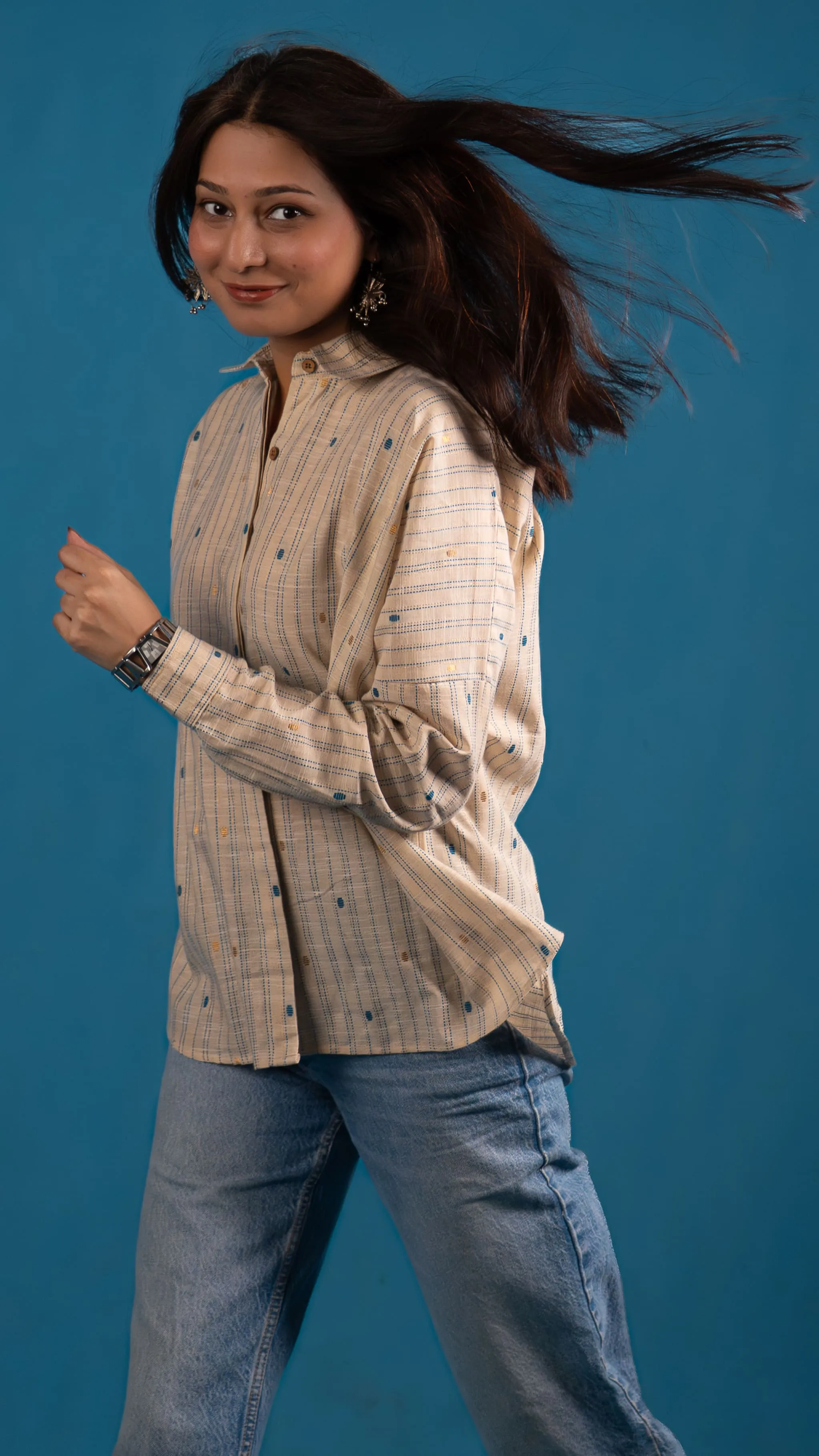 Woman in a cream striped button-up shirt with windblown hair for Indyvarna.