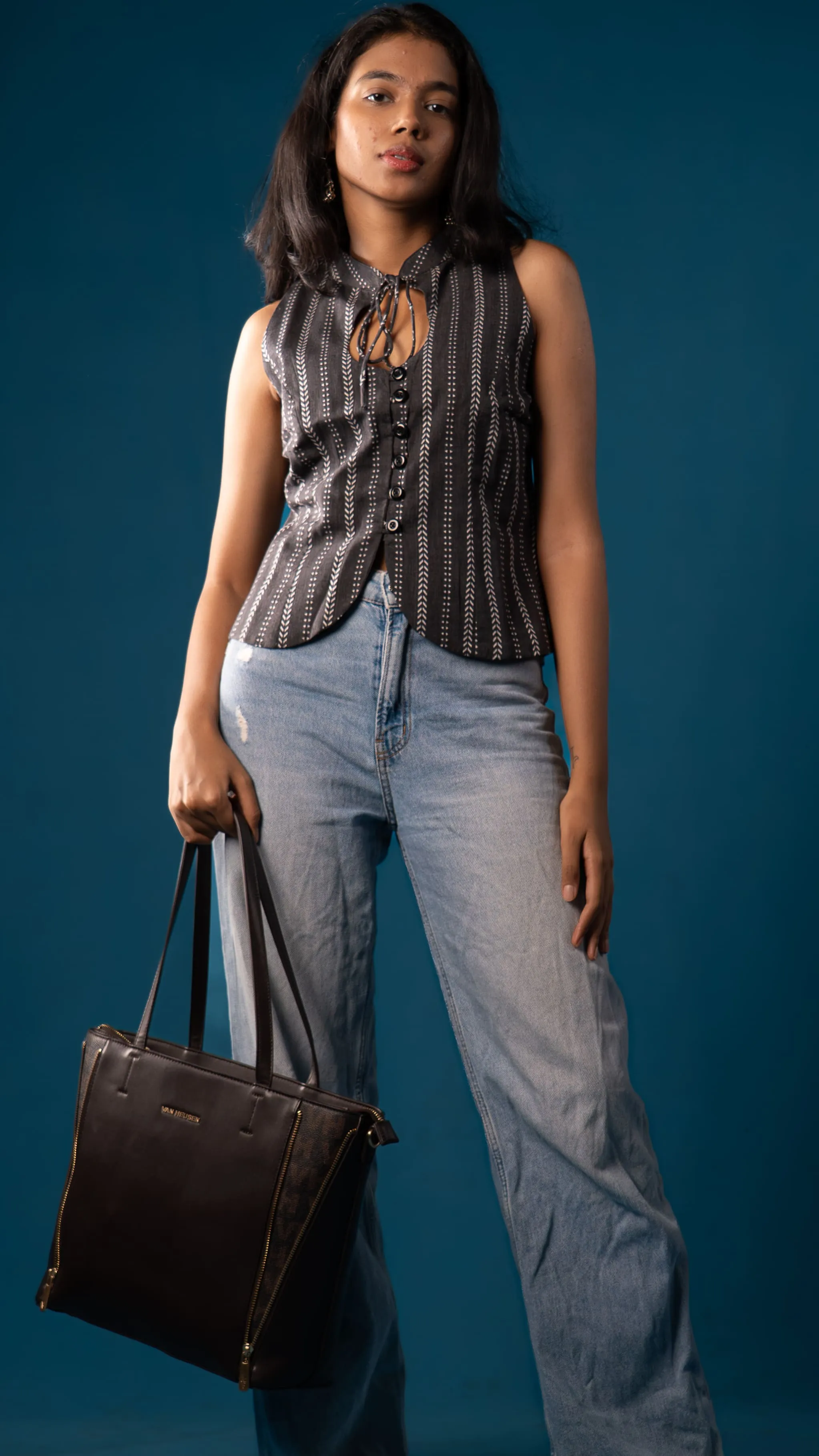 Woman in a black sleeveless patterned top holding a black tote bag for Indyvarna.