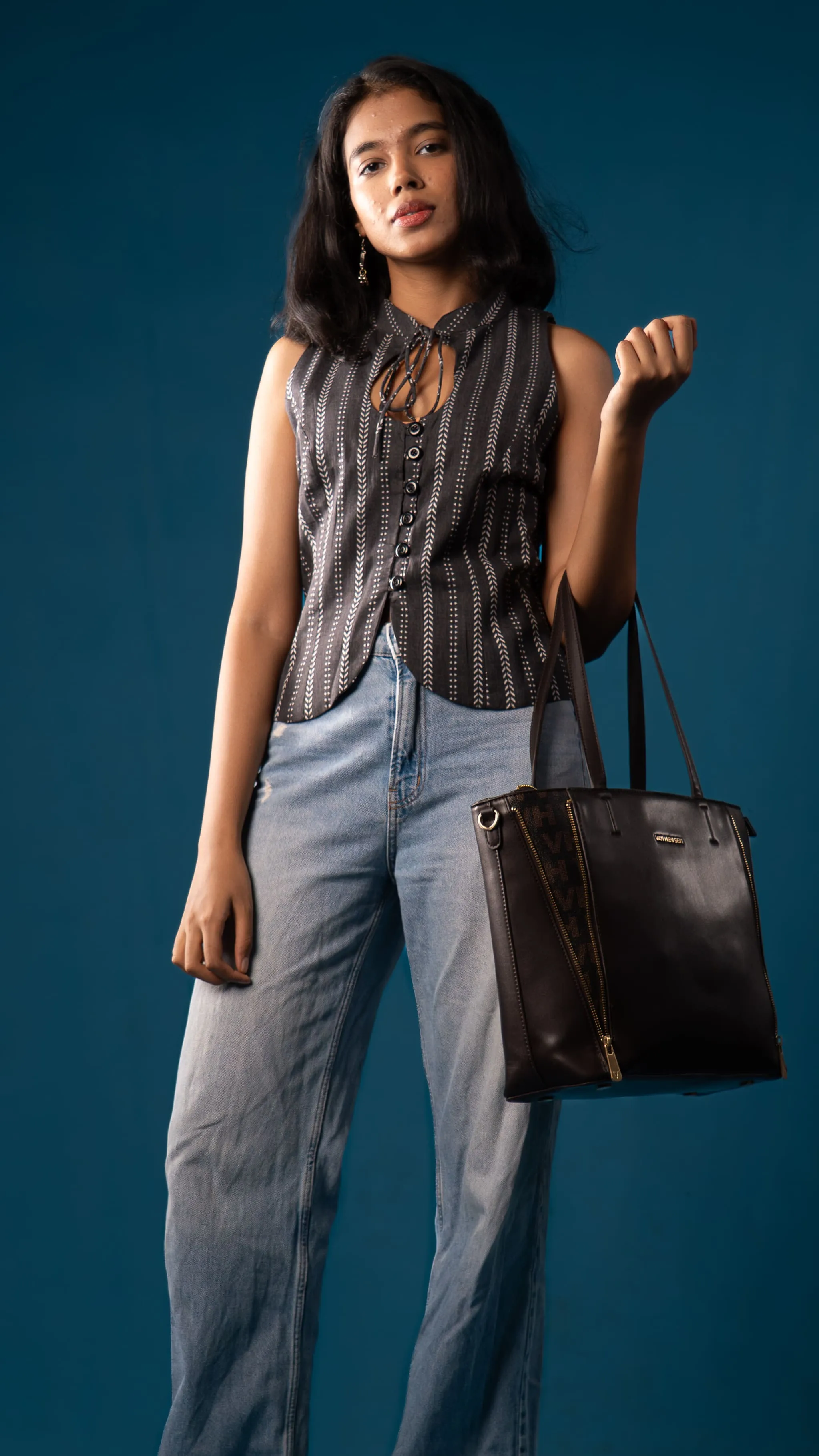 Woman holding a black tote bag with a black patterned sleeveless top for Indyvarna.