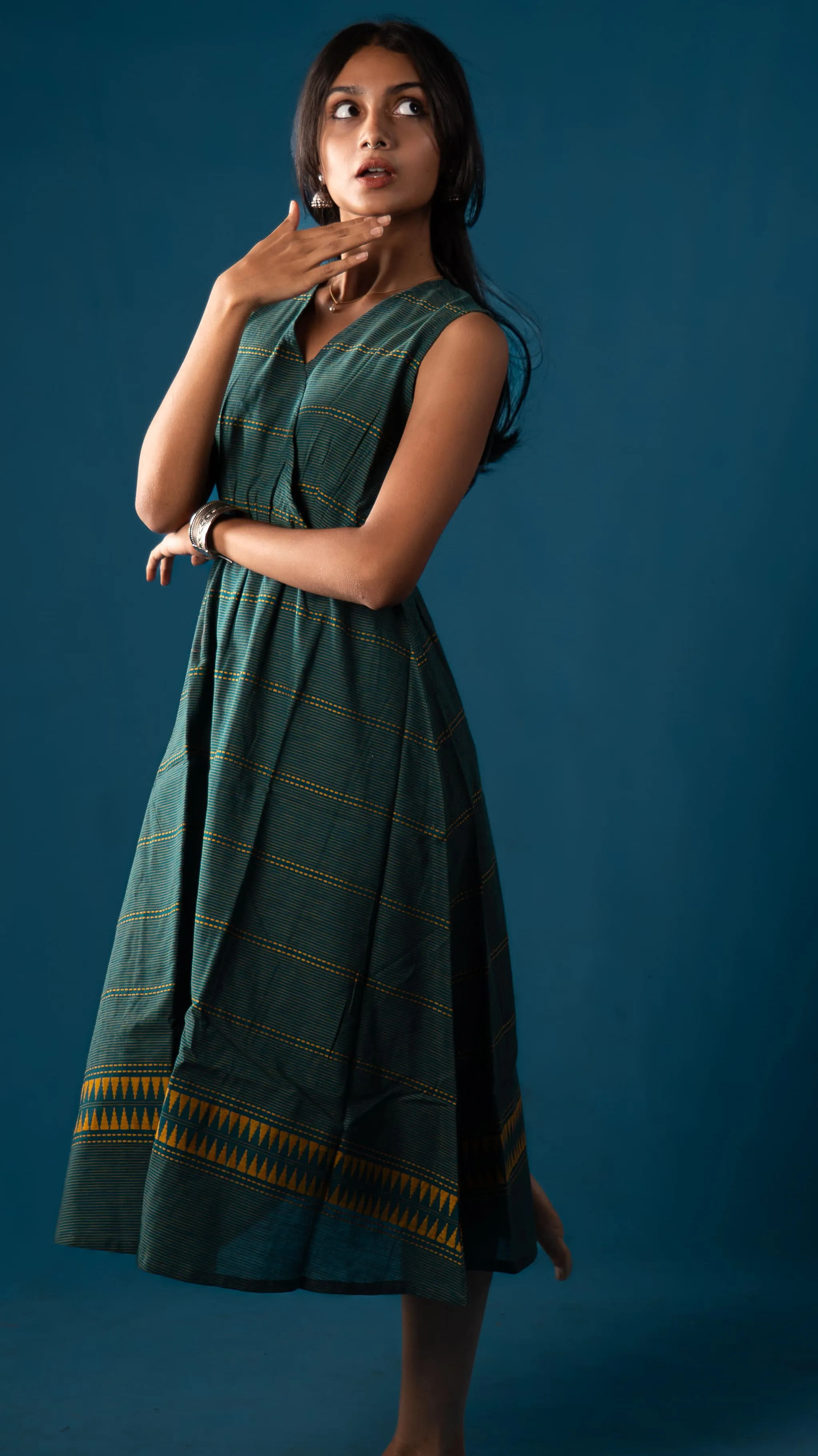 Woman in a green sleeveless dress posing against a blue backdrop for Indyvarna.