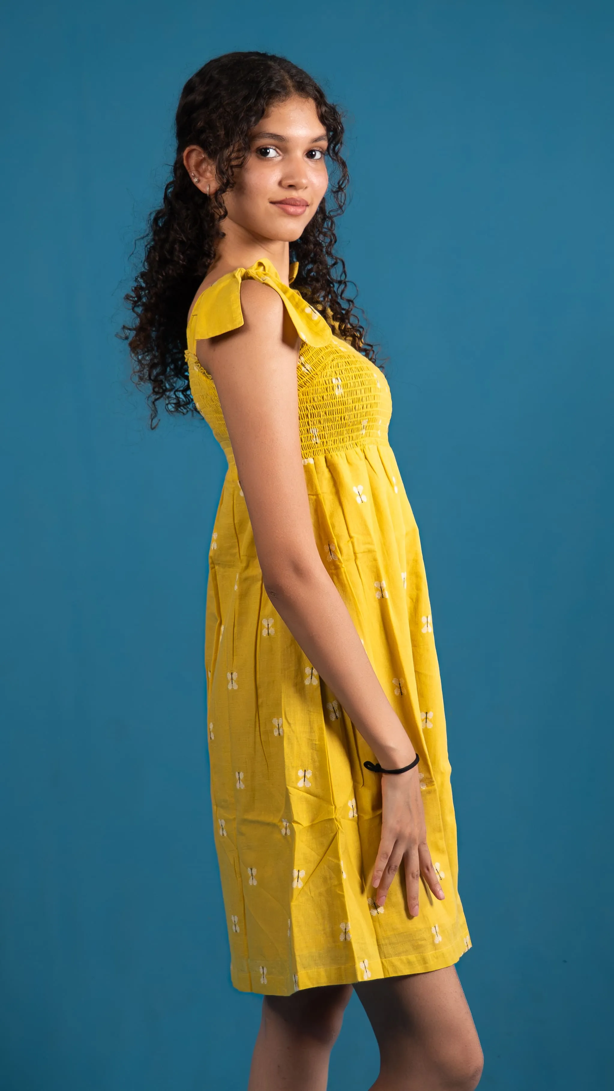 Side view of a yellow smocked dress with shoulder ties for Indyvarna.