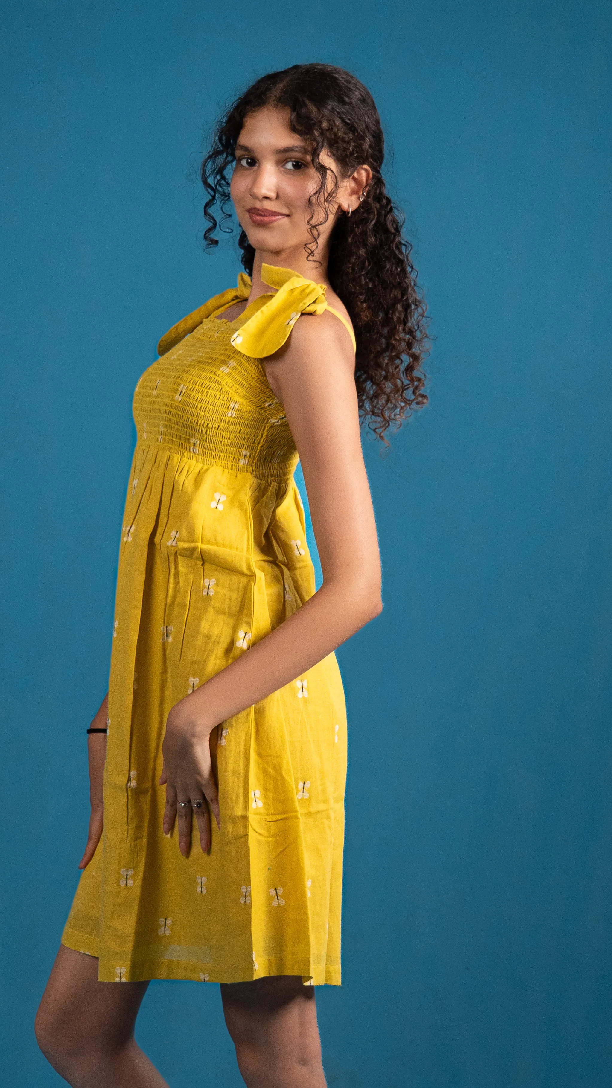 Woman in a yellow smocked dress with shoulder ties for Indyvarna.