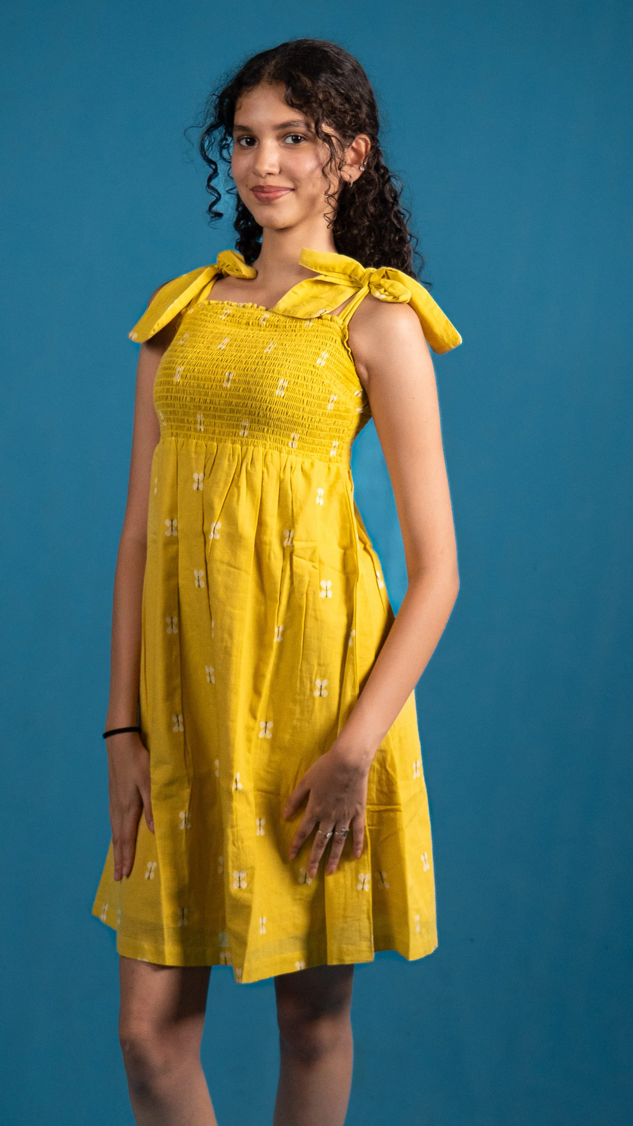 Woman in a yellow smocked dress with shoulder ties for Indyvarna.