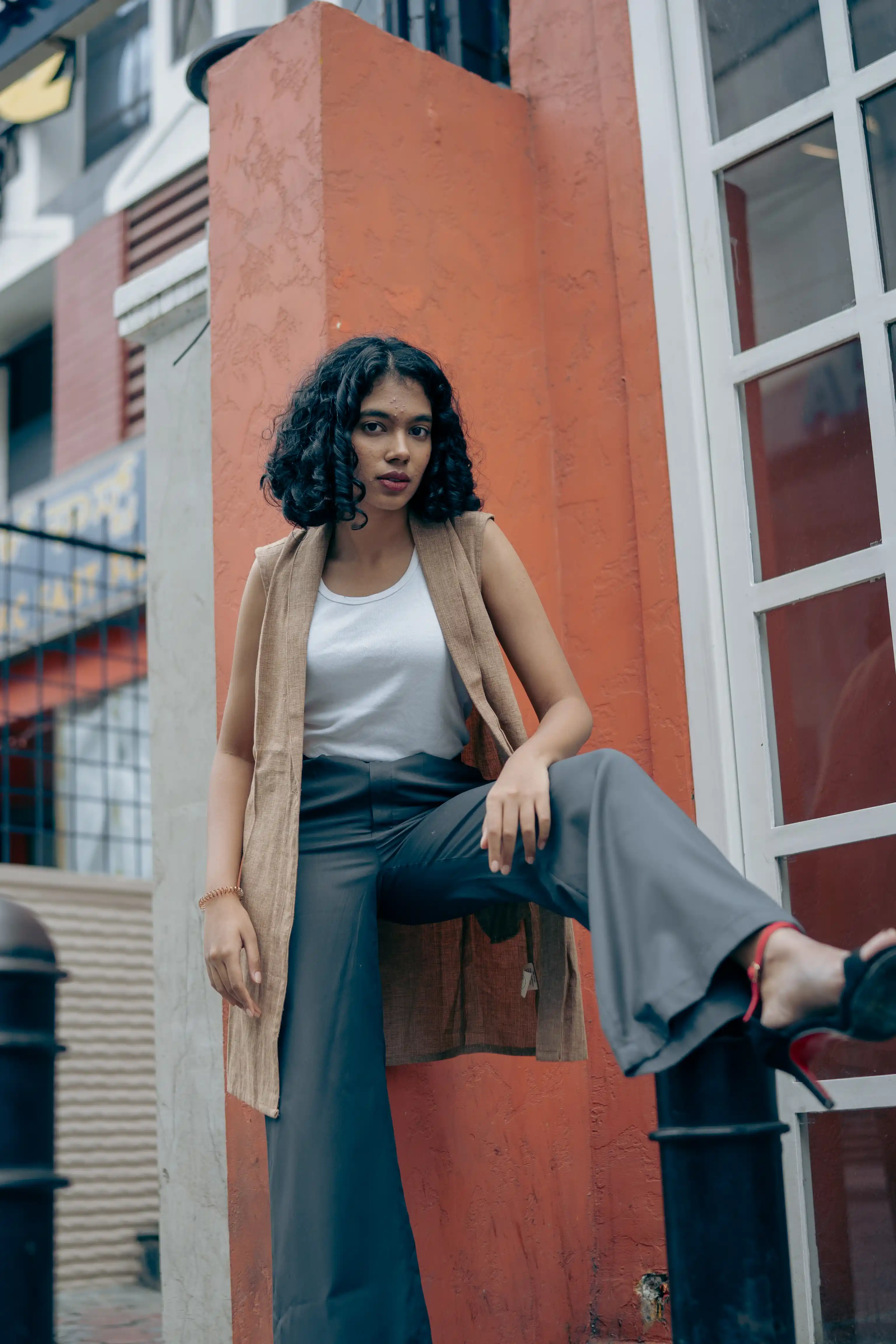 Woman in a long tan sleeveless vest and dark trousers for Indyvarna.