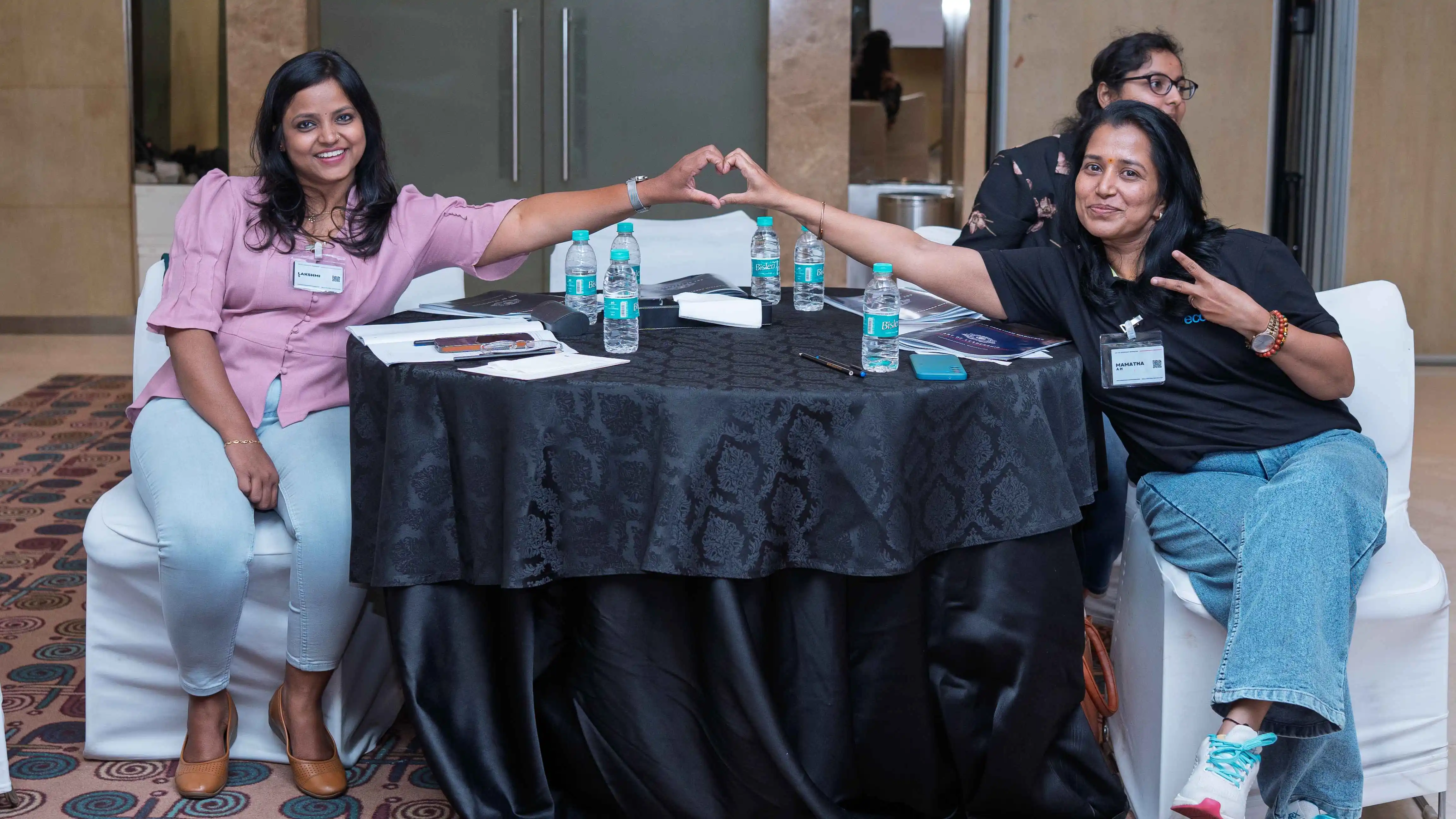 Two participants make a heart gesture at a Skill Beyond Education event table.