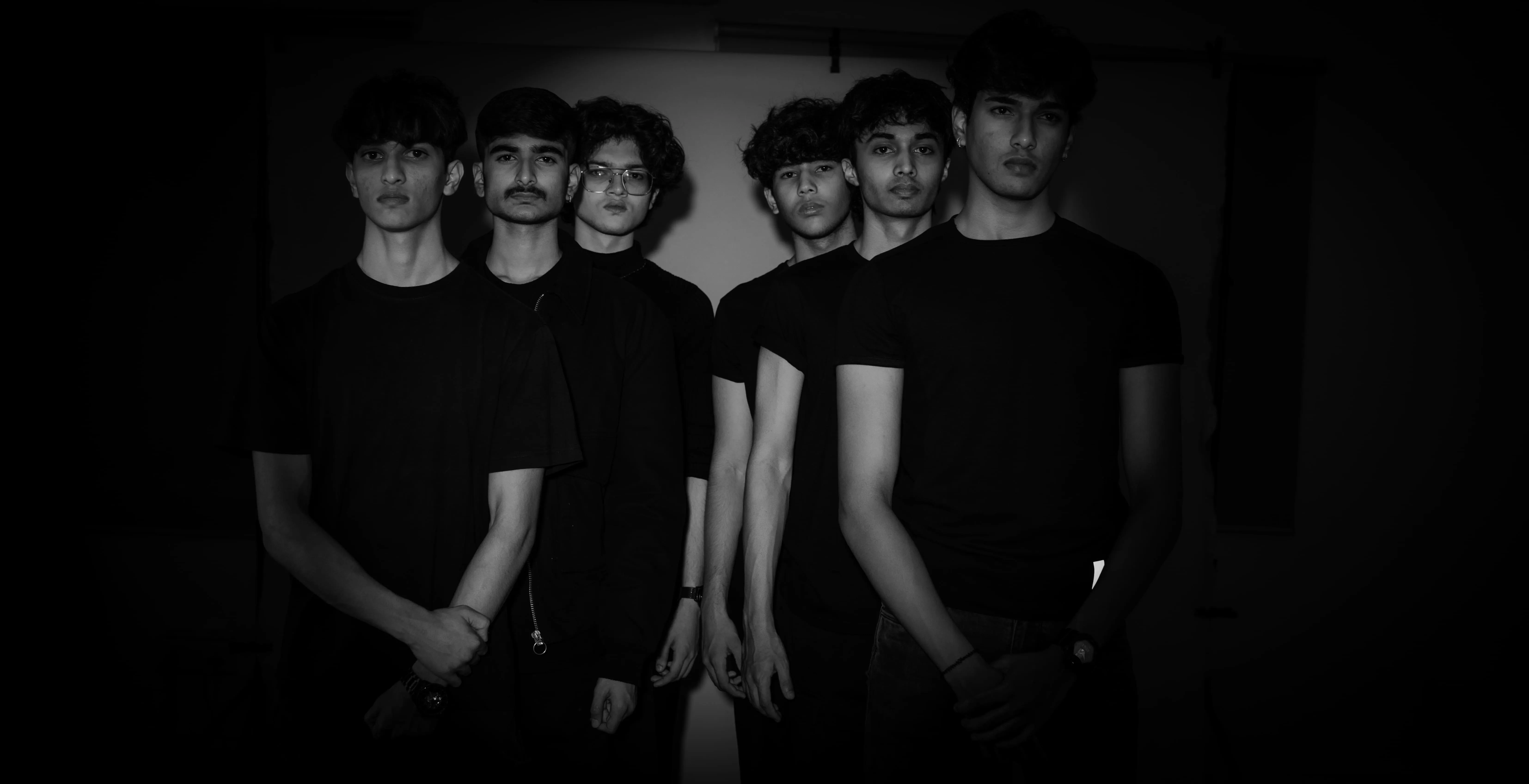 Seven men in black pose in a low-key studio portrait for a model team photography project.