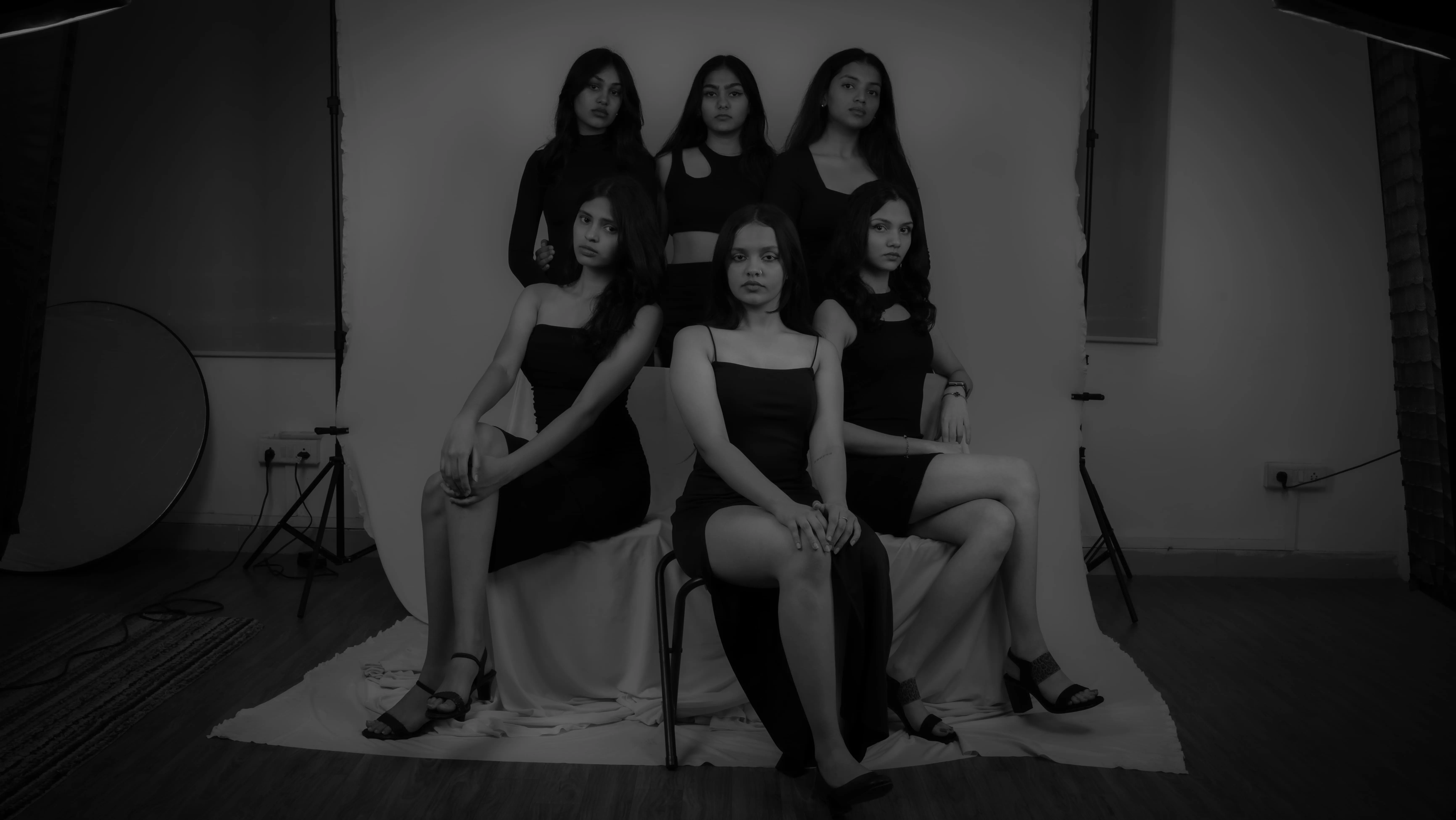 Six women in black dresses pose in a studio group portrait for a model team photography project.