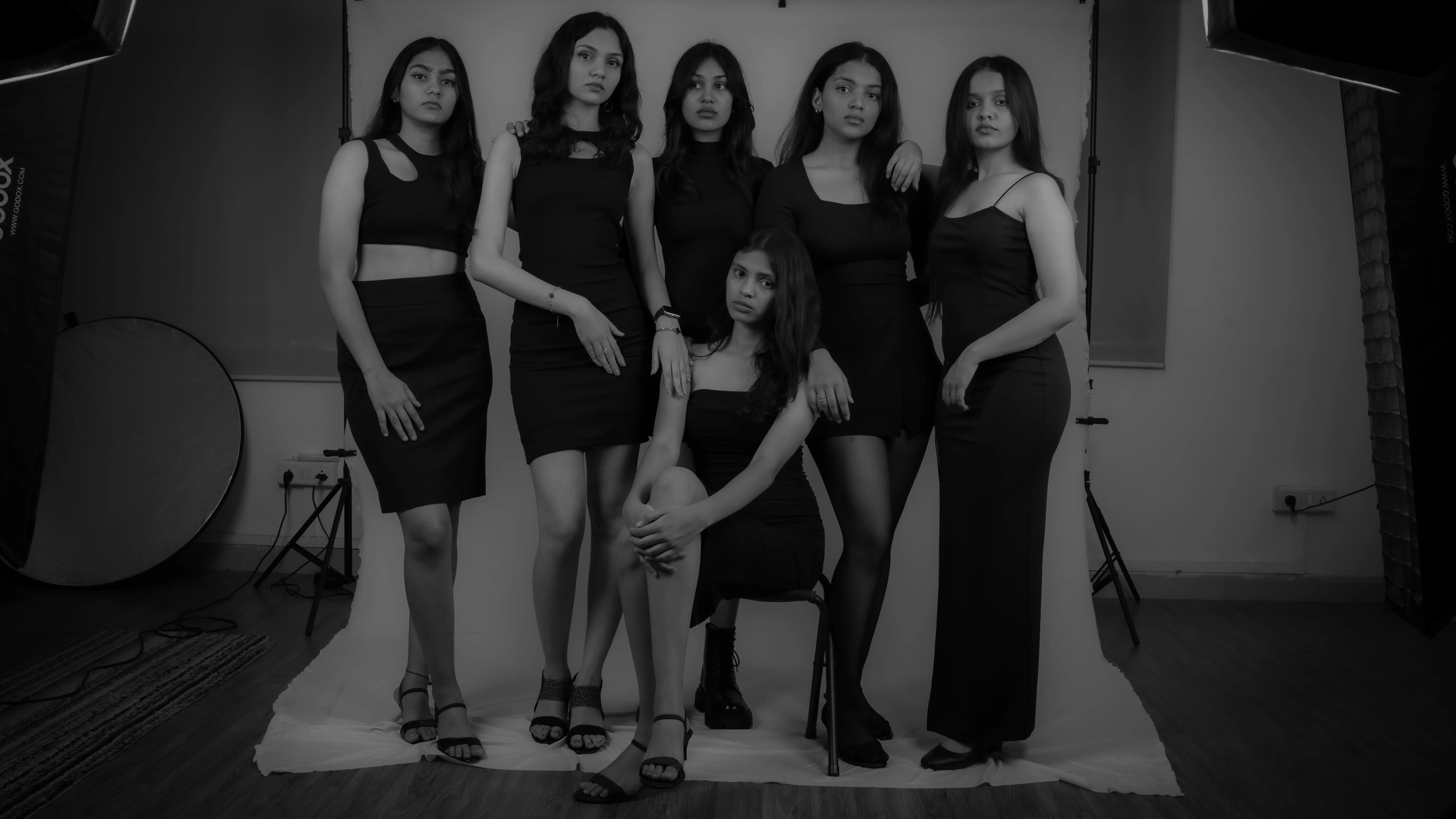 Six women in black dresses pose around a seated woman in a studio group portrait for a model team photography project.